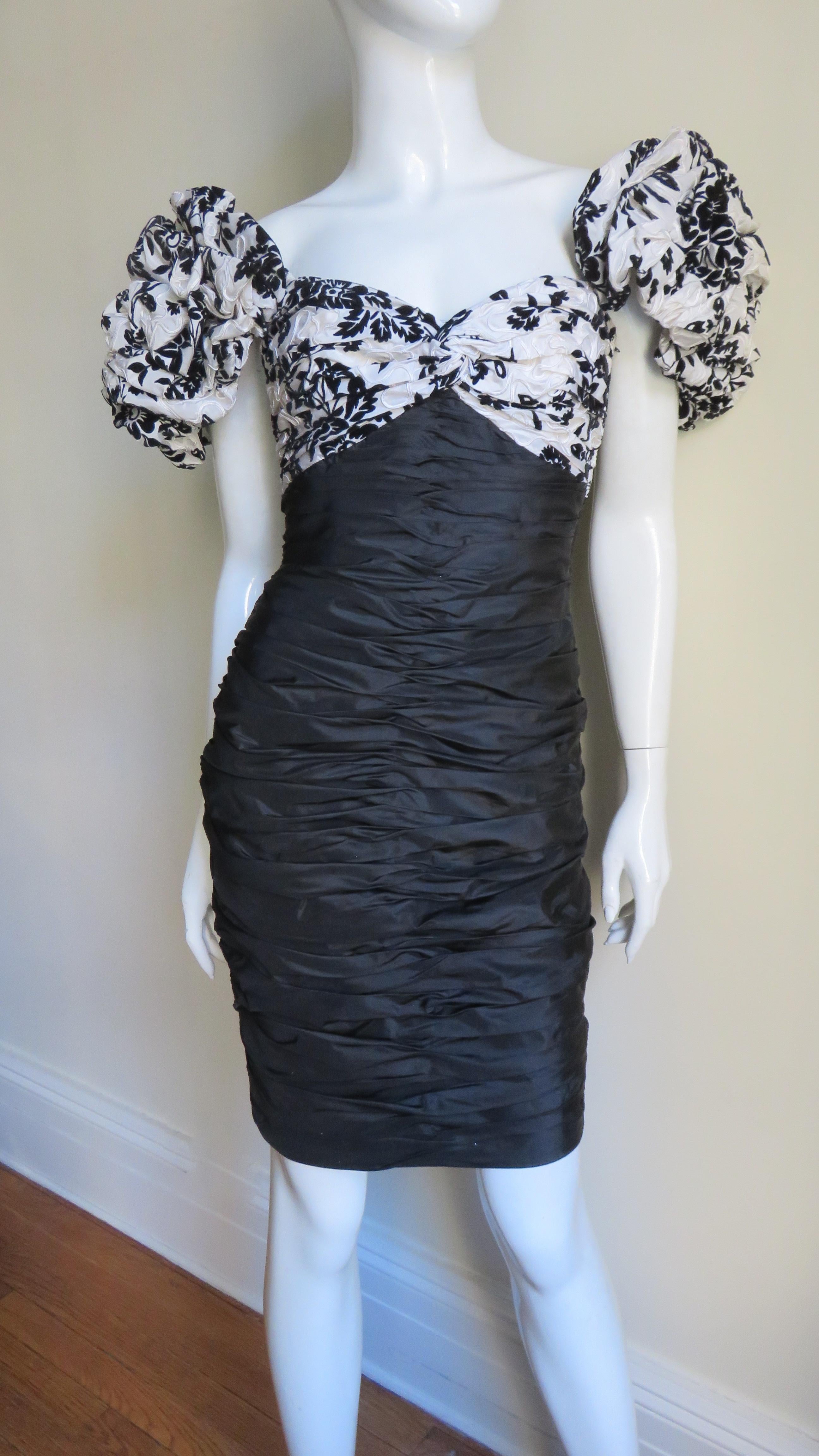 A beautiful black and white silk dress from Vicky Tiel's Couture collection.  It has a ruched sweetheart neckline, a scoop back, and puff short sleeves all in a black flocked flower pattern on a white background. The skirt portion is solid black and