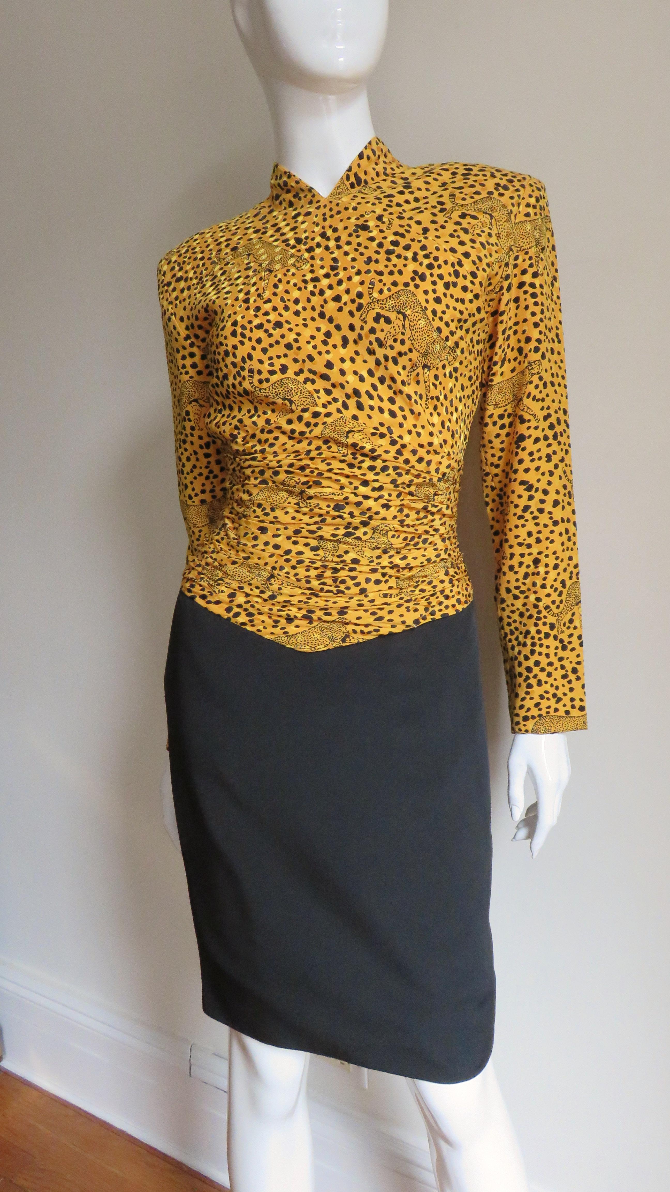 A great silk dress from Vicky Tiel Couture with a marigold bodice printed with leopards and a solid black skirt portion. The bodice has a small stand up collar, long sleeves, and horizontal ruching around the waist. The skirt portion is straight and