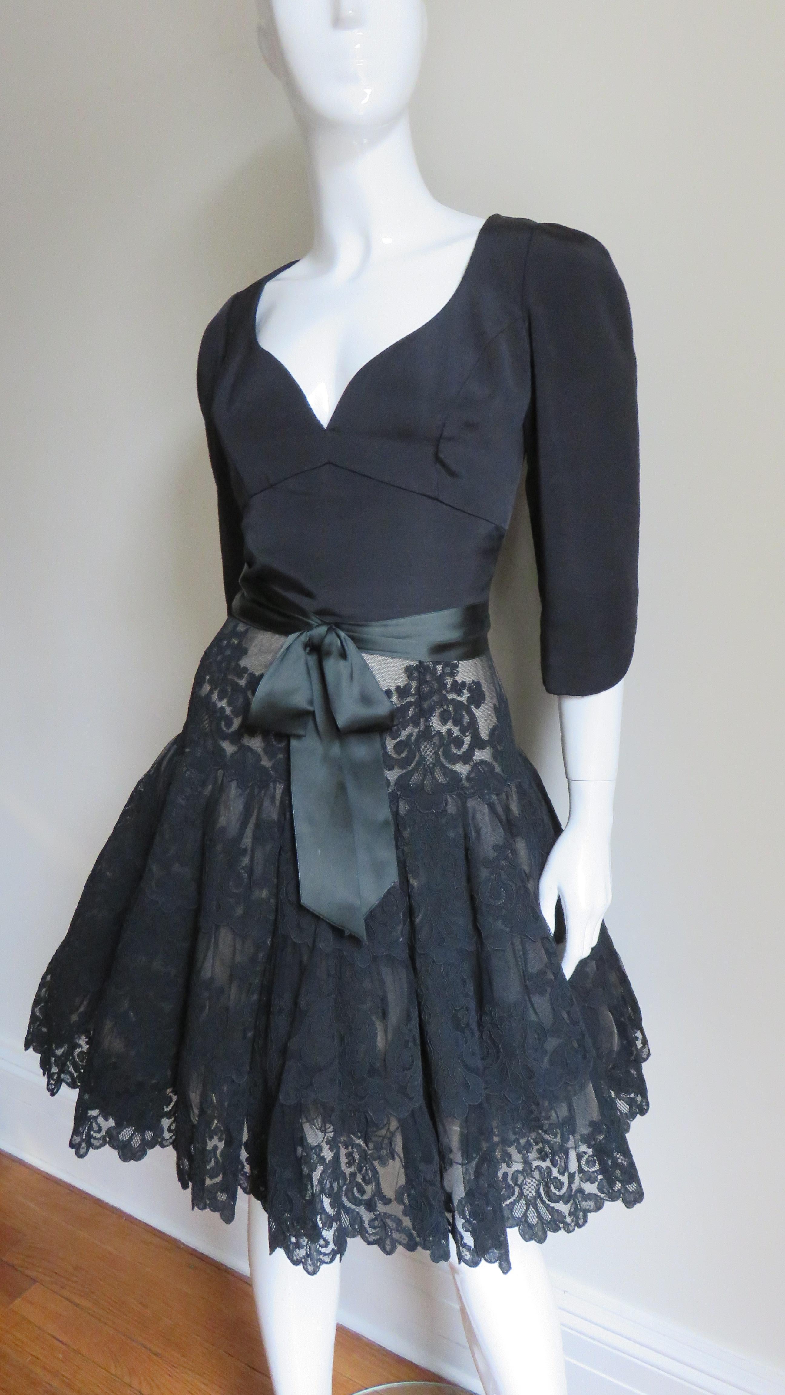 A gorgeous black silk and lace full skirted dress by Vicky Tiel.  It has a fitted silk bodice with a sweetheart neckline and notched elbow length sleeves.  The full skirt's top layer is beautifully detailed black lace with a scallop hemline and 4