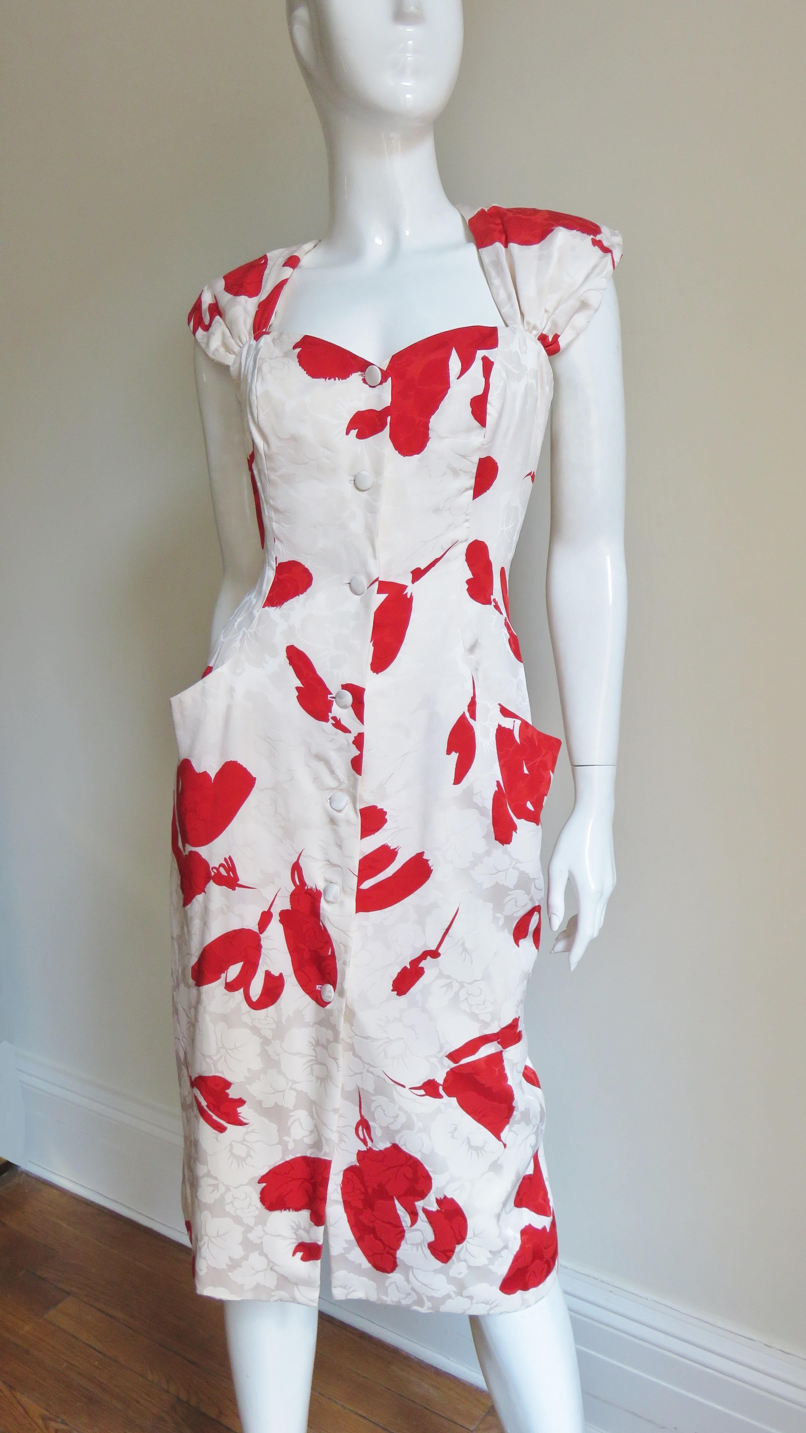 A beautiful off white silk damask dress with a red flower print from Vicky Tiel.  It has front pockets and closes with self covered buttons. The cap sleeves narrow and cross at the upper back and below them are 2 angled drapings at the waist.  It is