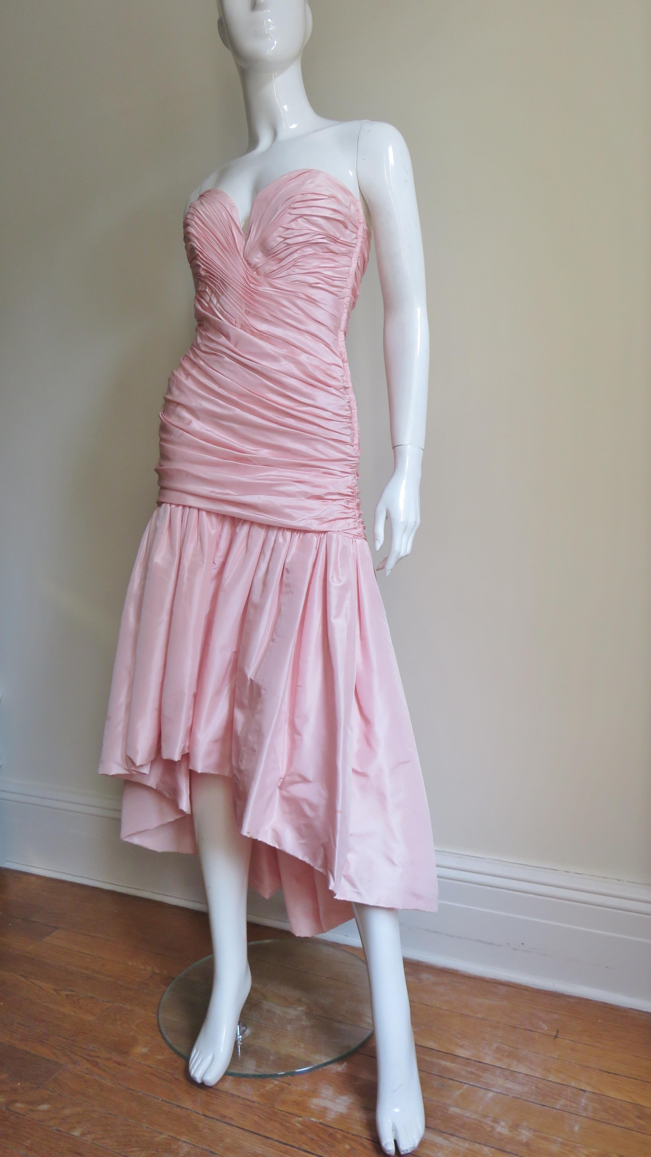 A great pink silk high low dress from Vicky Tiel. It has a drop waist horizontally ruched boned bustier bodice onto which is gathered a full skirt knee length in the front, ankle length in the back. The dress has a side zipper and is fully lined in