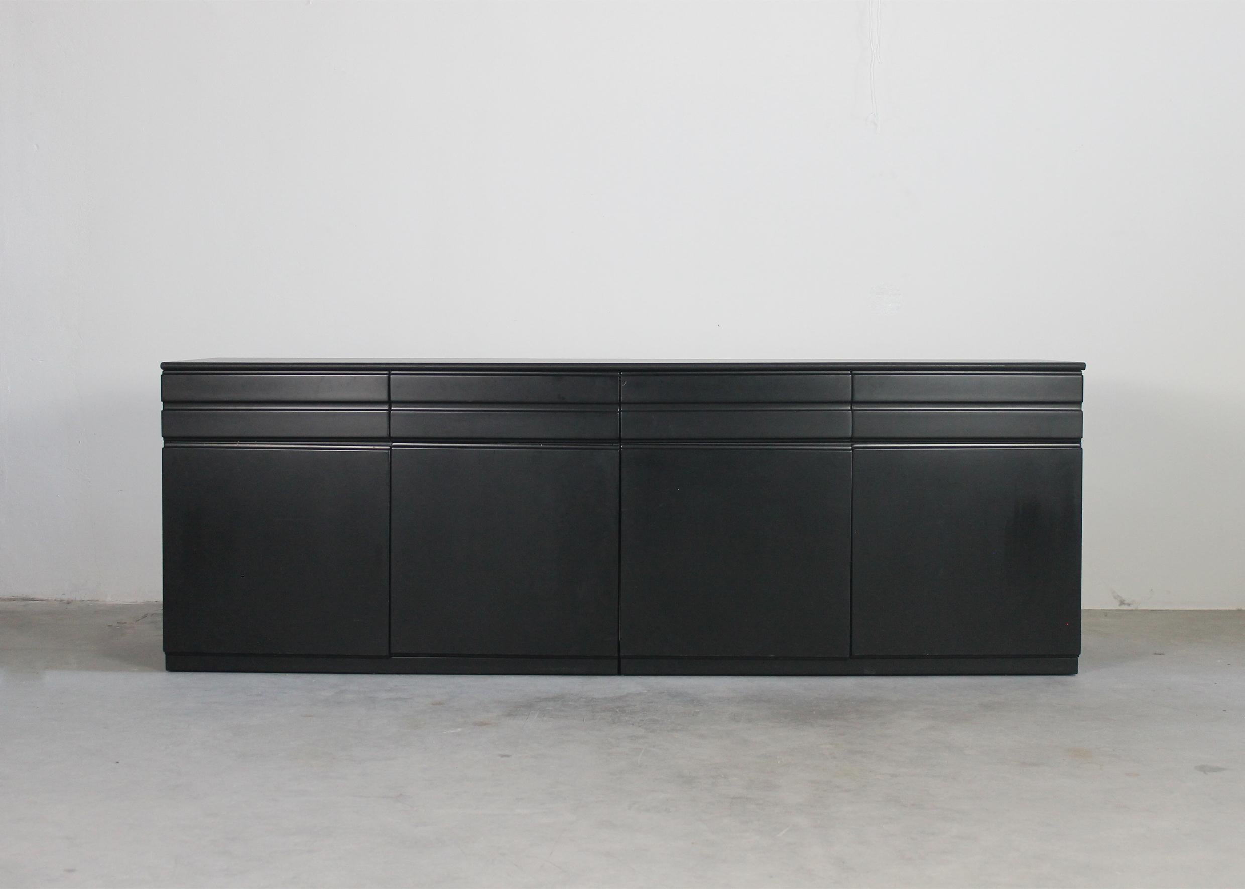 Commode modèle CS49 à quatre tiroirs frontaux et quatre portes avec étagères intérieures, structure en bois laqué noir et plateau revêtu de skaï noir ou de similicuir. 

Conçue par Vico Magistretti et produite par Poggi dans les années
