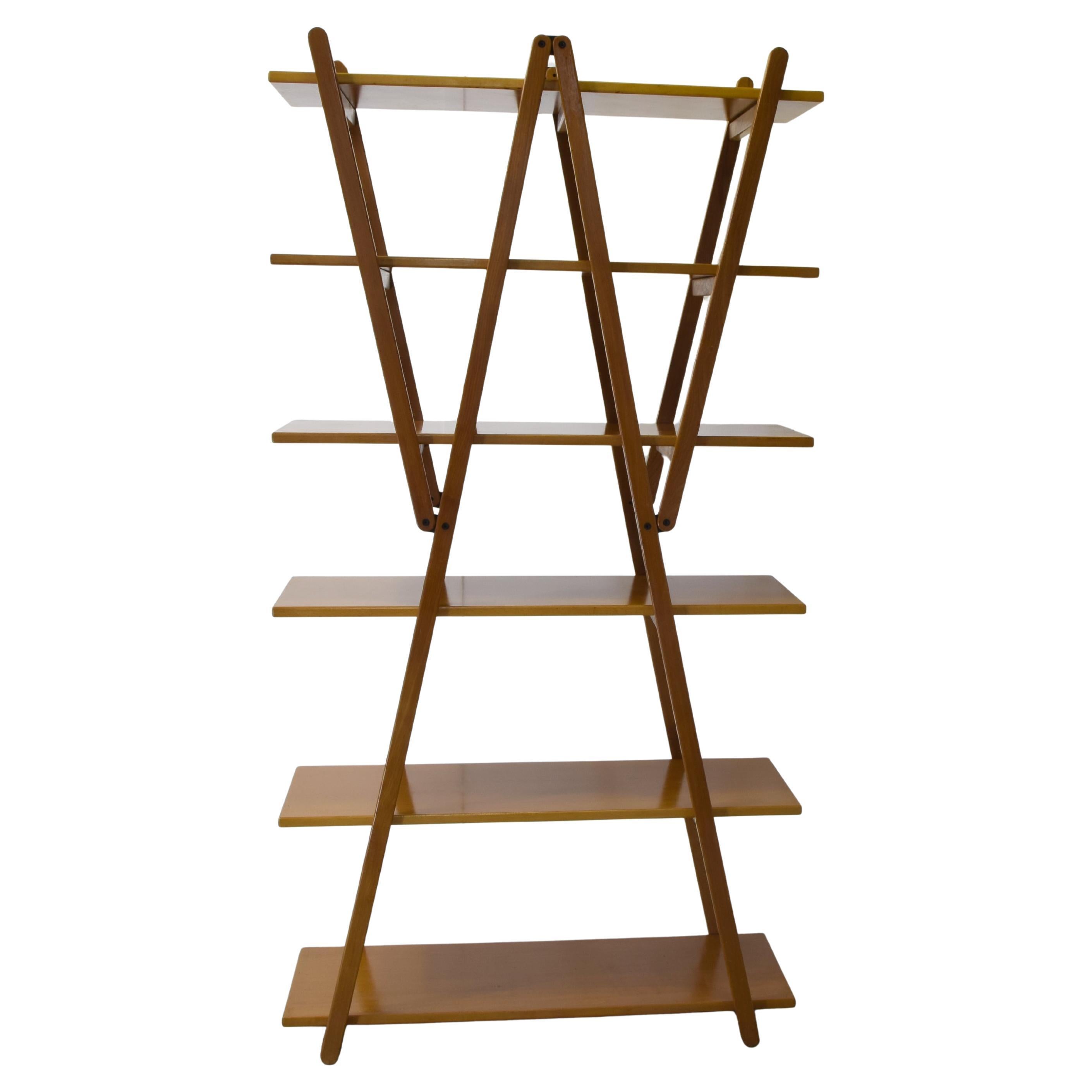 La libreria ha una struttura ridotta al minimo trasformando le diagonali in elementi portanti che permettono di eliminare i fianchi e di enfatizzare il ruolo delle cerniere nel dinamismo di un design iconico e senza tempo. Struttura in faggio
