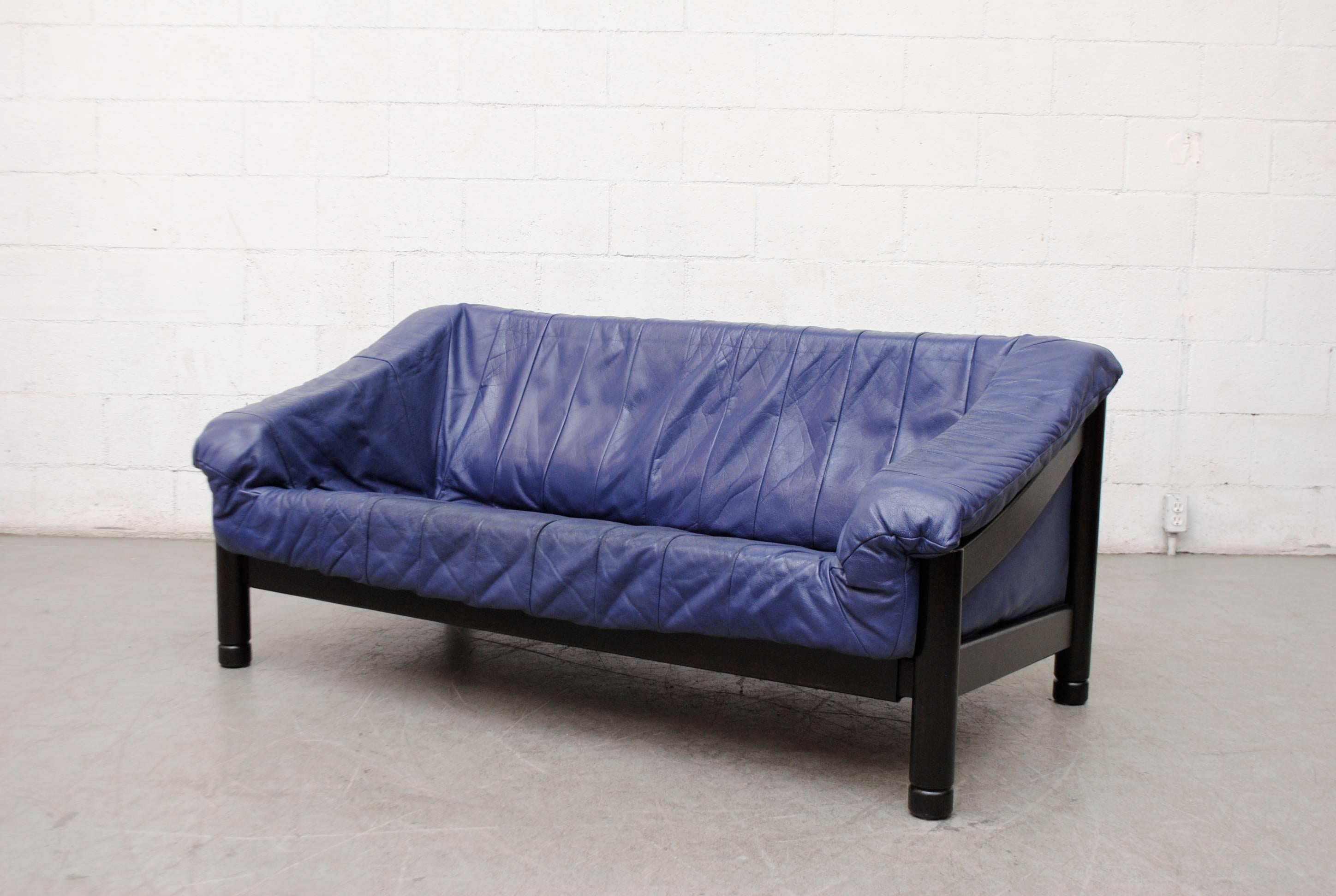 Handsome loveseat with lightly refinished, ebony stained wood frame and cobalt blue leather bucket insert cushion. Good original condition with signs of wear consistent with its age and usage.
