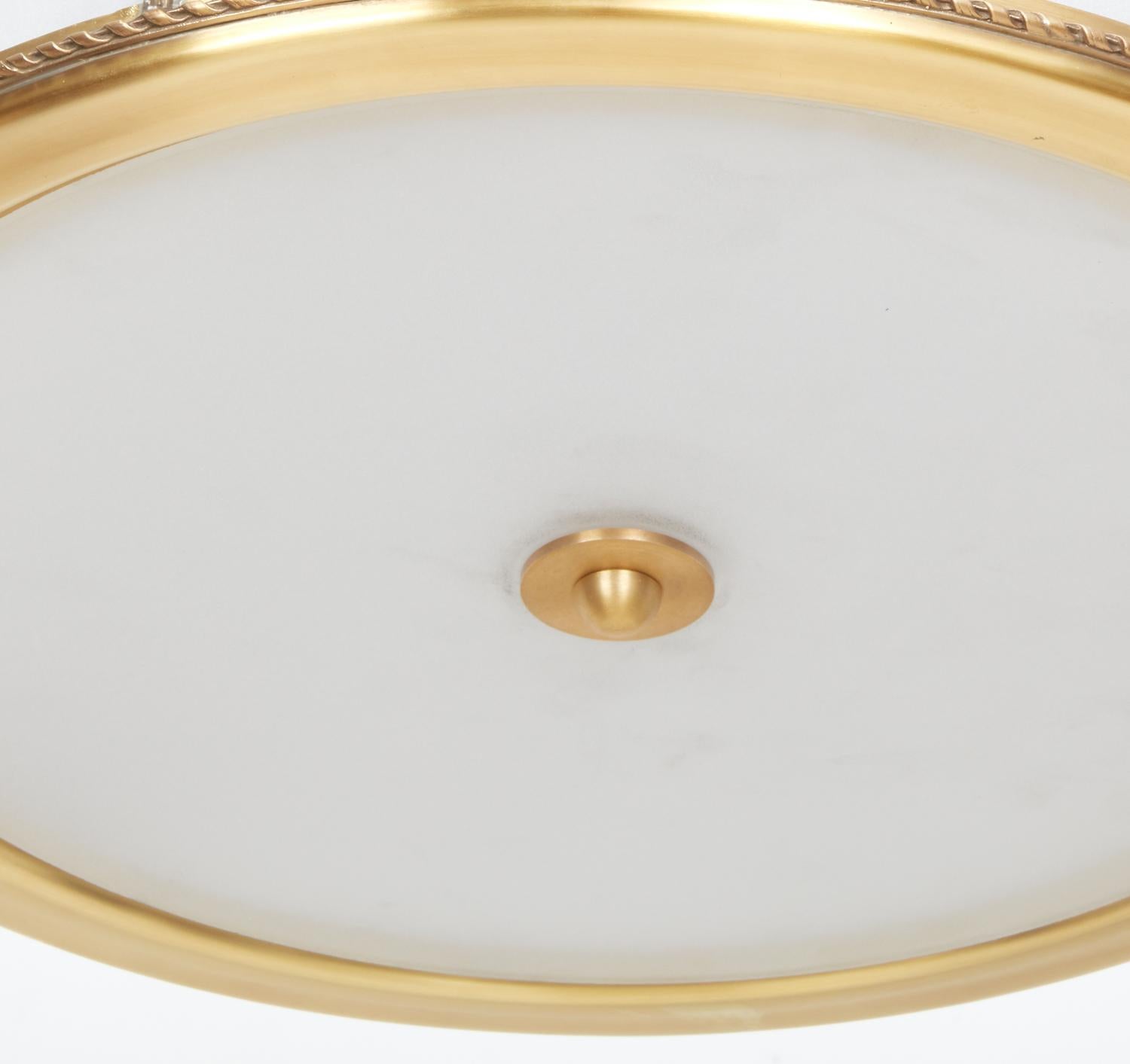 The Victoire flush mount in brass, designed by David Duncan. The round frame having curved, low iron glass in three sections, separated by rectangular sections with beveled edges under hand carved rock crystal rosette ornaments. Four Edison sockets