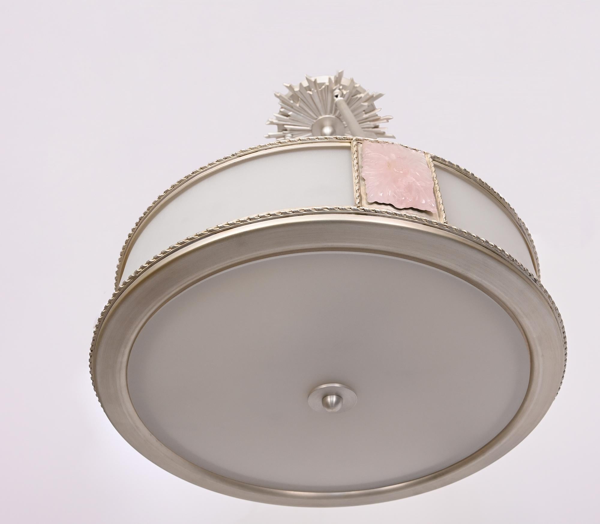 A custom, pendant light fixture with curved frosted glass sides and underside. The Victoire Rose Pendant Light features pink quartz roses, and a silver plate finish suspended by three rods, and cast nickel sunburst adorning the canopy. Four Edison
