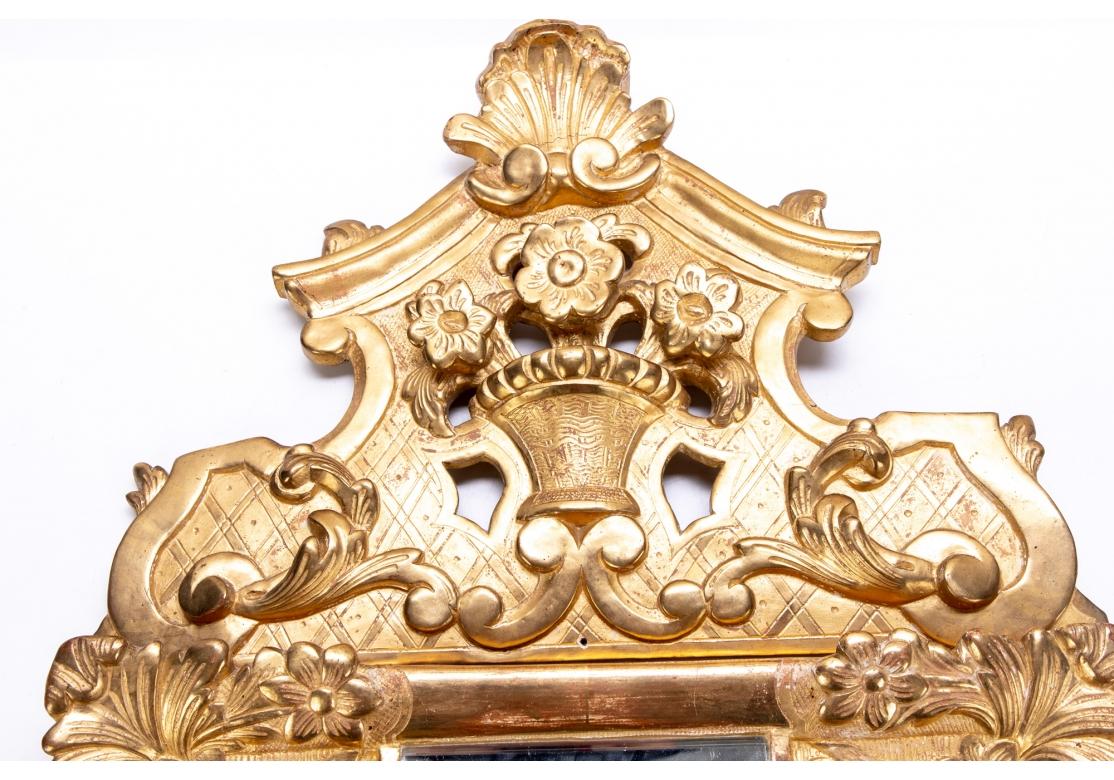 A French giltwood mirror with a deep relief flowering basket crest with shell on top, the mirror with foliate and floral motif corners separated by 