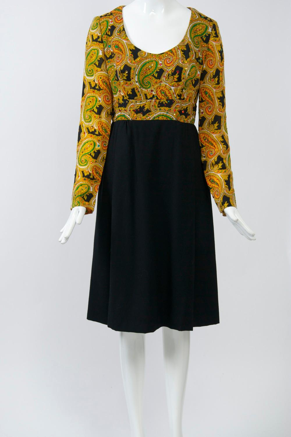 c.1970 dress by Victor Costa featuring a modified empire bodice of paisley wool challis has a scoop neck and is sprinkled with coordinating  red and green rhinestones. The set-in paisley waistband gives way to a black knit A-line skirt with soft