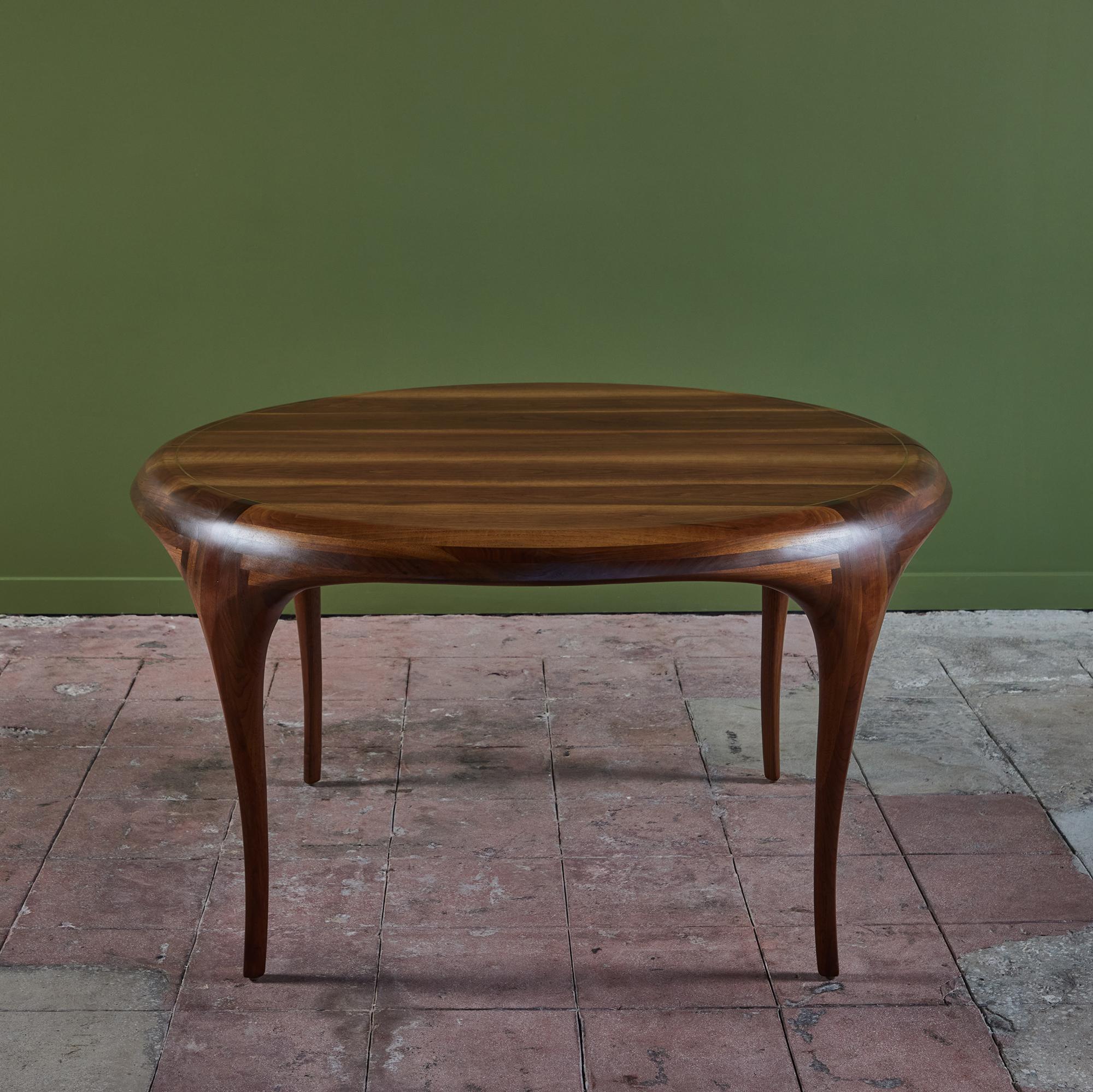 American made walnut dining table, c.1985, by Santa Barbara California craftsman Victor Dinovi. The table features a round top situated on four tapered sculpted legs. The table has two leaves which extend to a 93