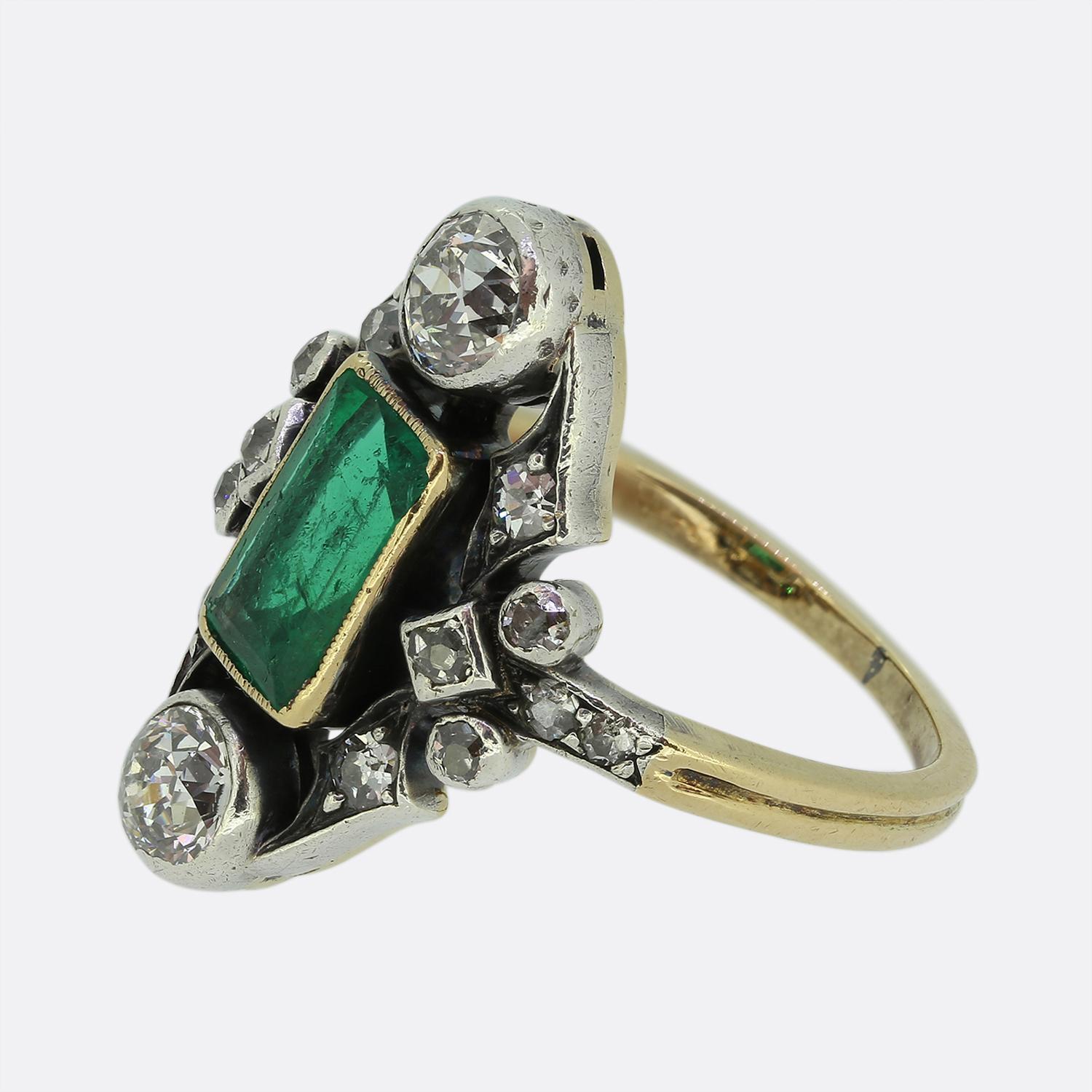 Hier haben wir einen wunderschönen Cluster-Ring aus der viktorianischen Ära. Dieses antike Stück wurde aus 18 Karat Gelbgold gefertigt und zeigt einen länglichen Smaragd im Smaragdschliff, der einen mittelgrünen Farbton hat. Dieser Hauptstein wurde