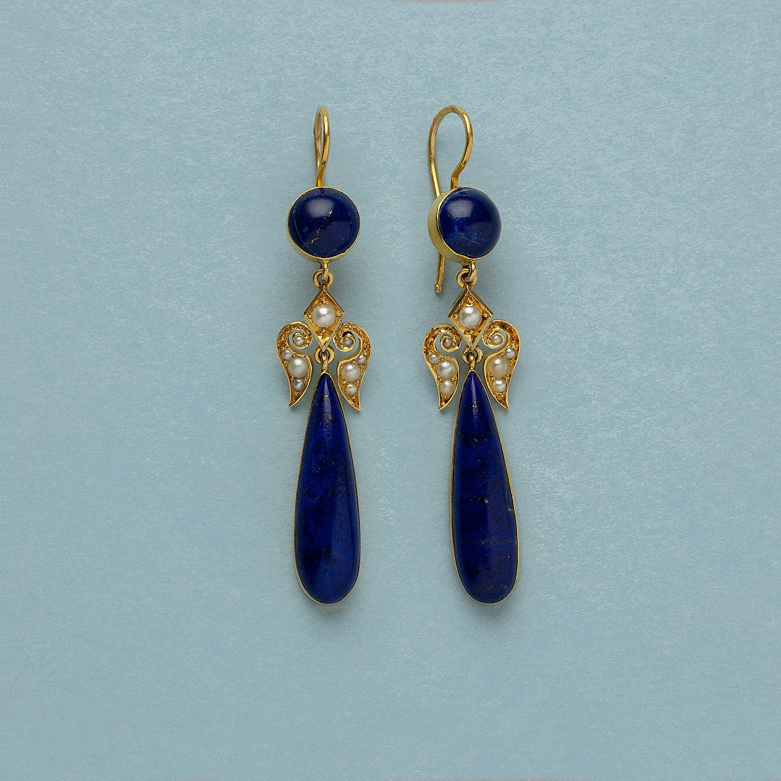 A pair of 14 or 15 carat gold earrings with a round cabochon cut lapis lazuli in a gold setting, below is a fleur de l’ys set with pearls, and a dangling pendant with a long pear shaped lapis lazuli, England, end 19th century.

weight: 10.84