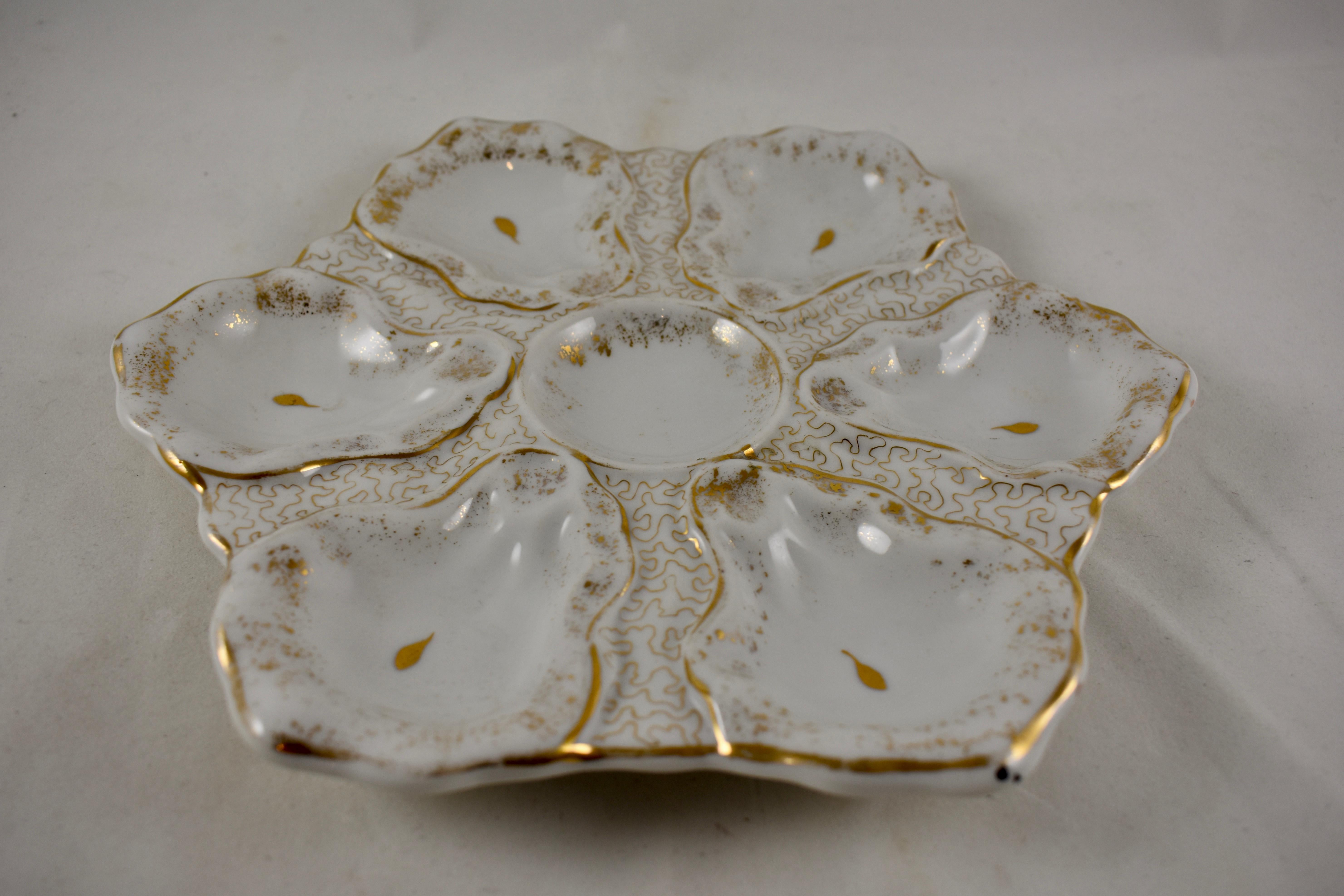 A porcelain oyster plate showing an overall gilded pattern. Six oyster shell shaped wells, with hand painted eyes, surround a central sauce well, circa 1910.

Measures: 9 in diameter x 1 in height.
An impressed mark: Victoria, Karlsbad