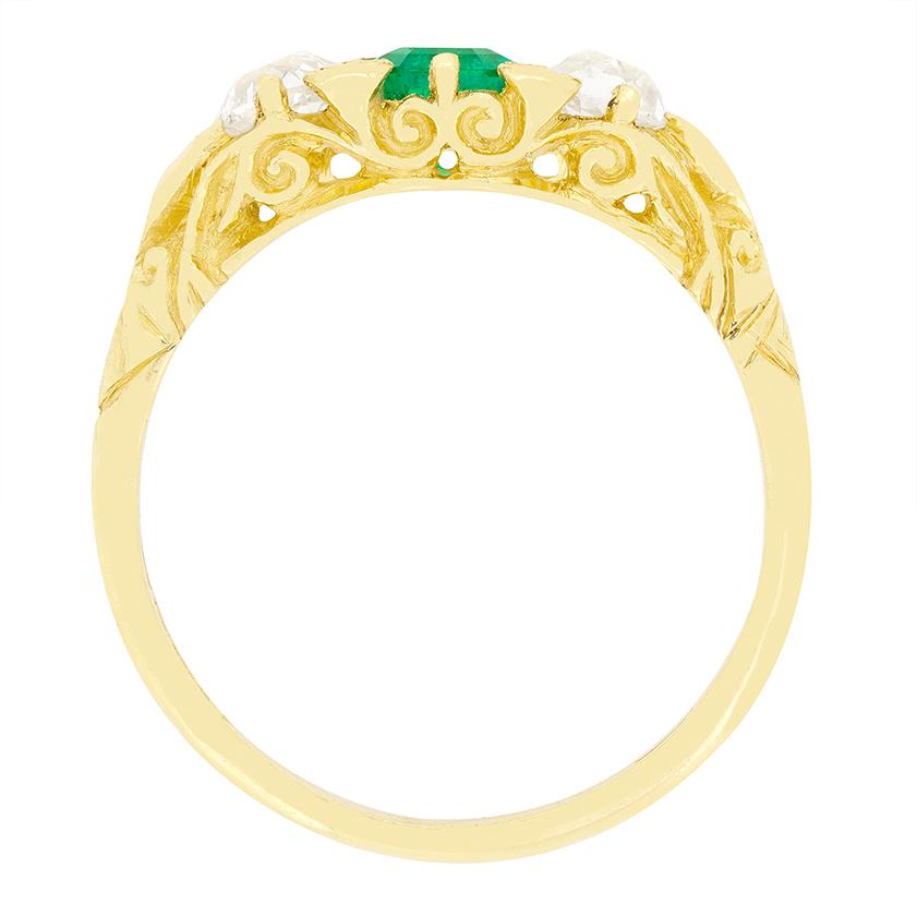 This beautifully carved shank trilogy ring dates back to the Victorian era. Taking centre stage, a stunning emerald cut Emerald is flanked by two old cut diamonds. The central Emerald weighs 0.50 carat and is a natural Columbian stone. The two