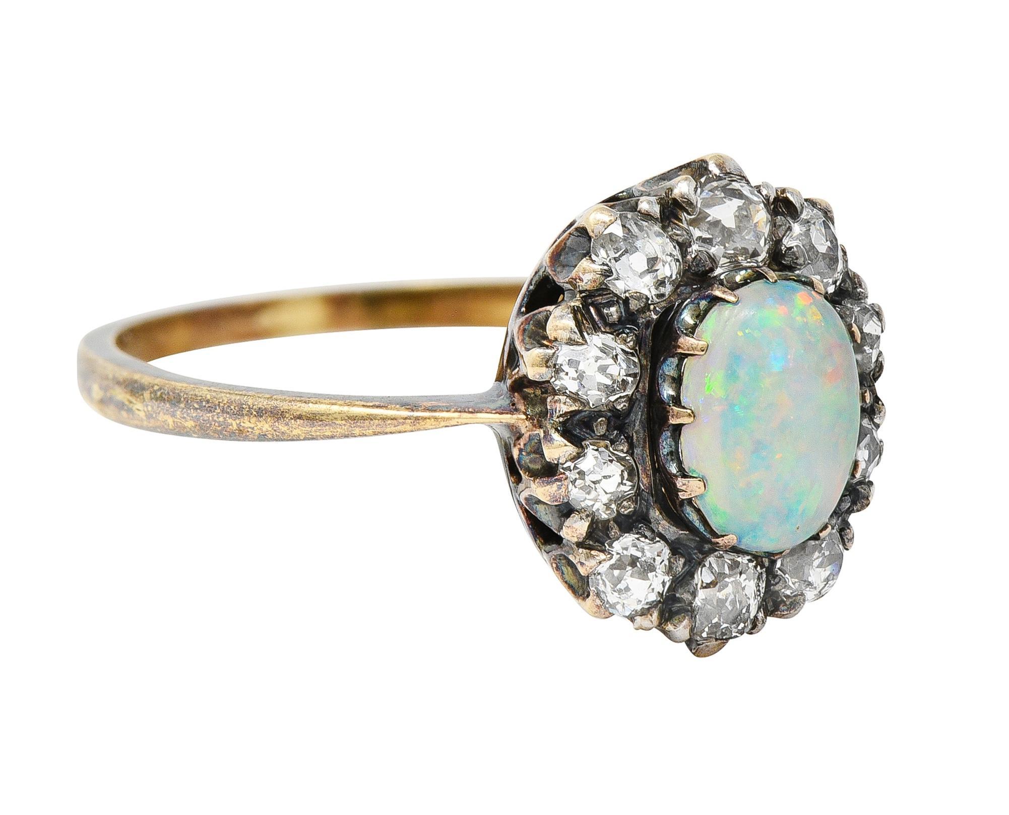 Centering an oval shaped opal cabochon measuring 6.5 x 5.0 mm 
Translucent white body color with spectral play-of-color
With a recessed halo surround all prong set in silver-topped gold
Halo is comprised of old mine cut diamonds 
Weighing