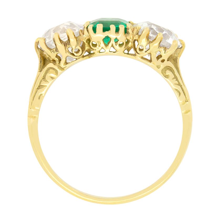 This exquisite Victorian carved shank trilogy ring features a stunning Columbian emerald at its centre. The emerald is 0.80 carat in weight and cut in a classic emerald cut shape. Flanking the ruby are two 1.25 carat old cushion cut diamonds, which