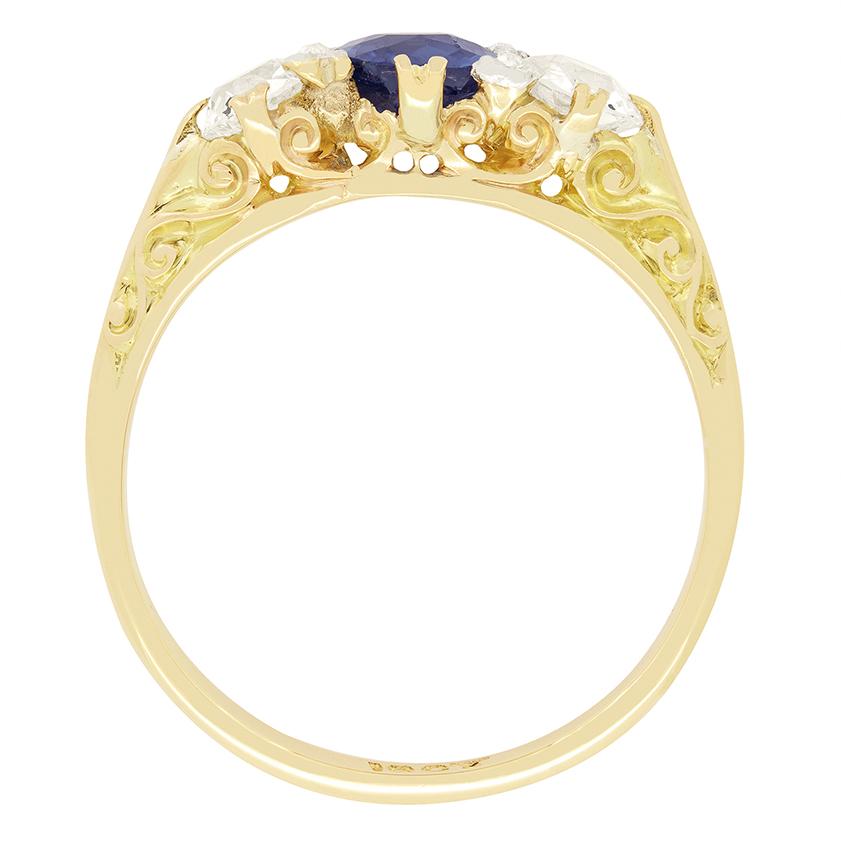 This beautiful Victorian era trilogy ring showcases a vivid blue old oval cut sapphire at its centre. The Sapphire is 0.85 carat and completely natural. On either side, two 0.50 carat old cut diamonds provide a brilliant contrast, each matching in