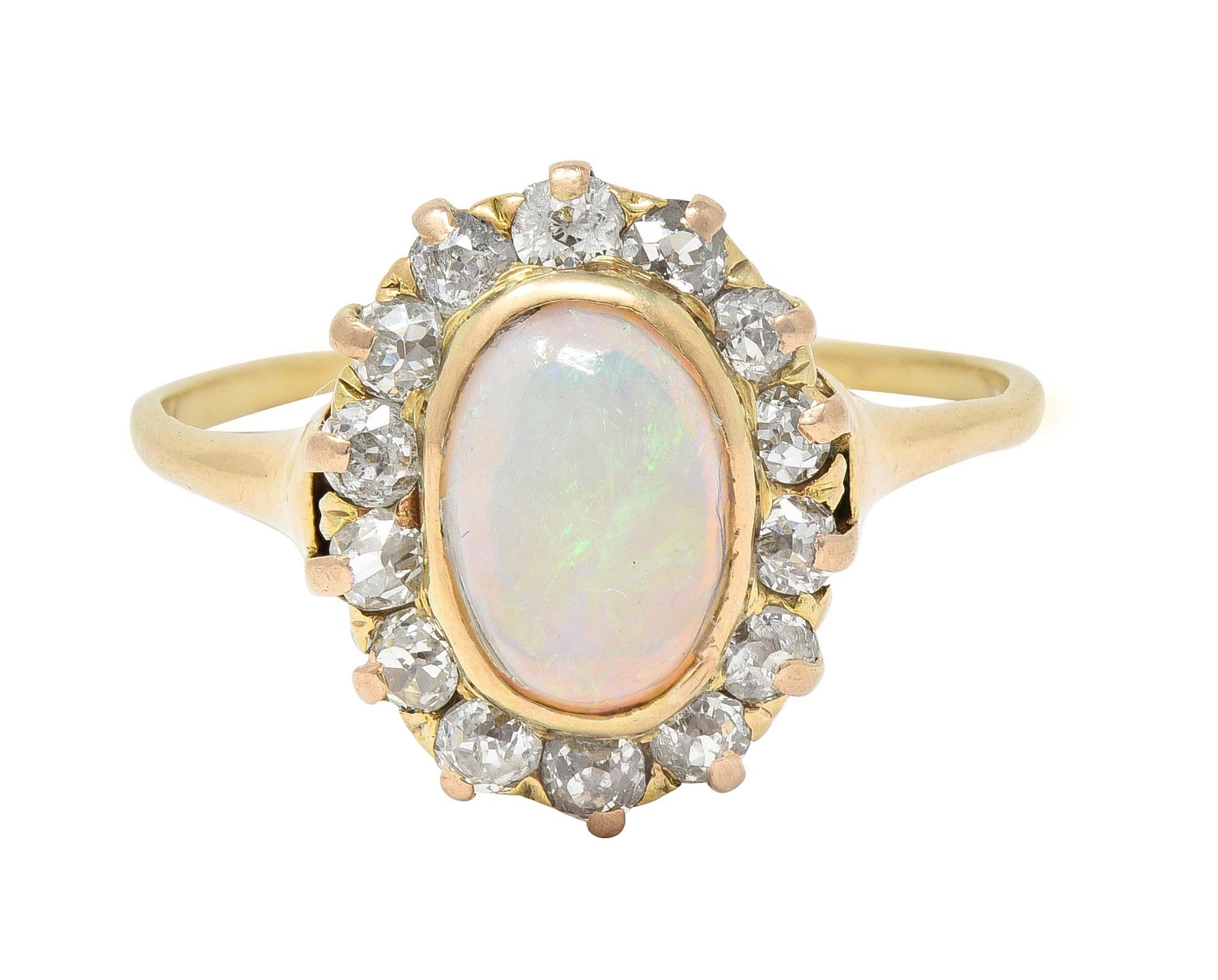 Centering an oval-shaped opal cabochon measuring 6.0 x 8.0 mm 
Translucent white in body color with spectral play-of-color - bezel set
With a halo surround of old mine cut diamonds with one transitional cut diamond 
Weighing approximately 0.86 carat