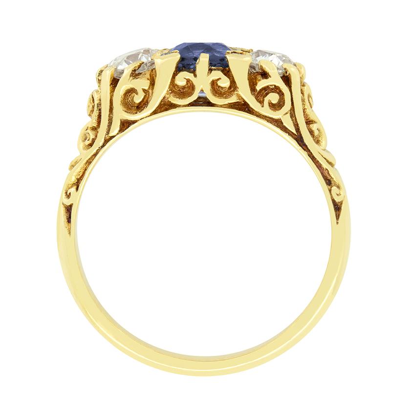 Un saphir bleu bleuet est flanqué de diamants de taille ancienne dans cette bague victorienne classique à tige sculptée. Le saphir central est une pierre de taille ovale pesant 0.90 carat. Les diamants qui l'accompagnent pèsent 0,40 carat chacun et