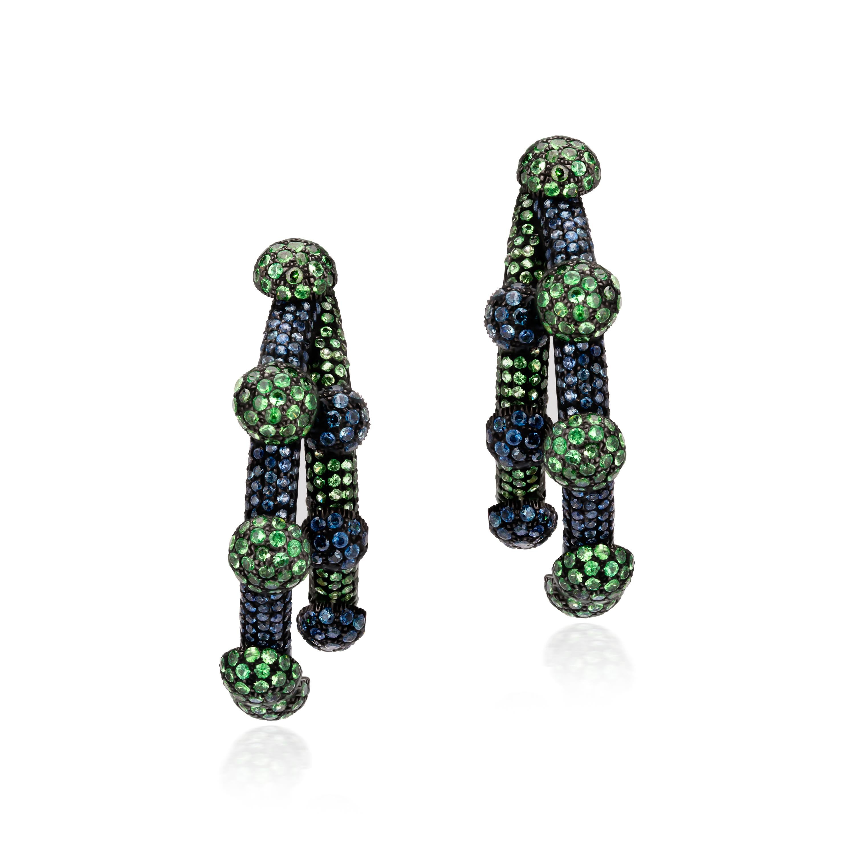 Illuminate your earlobes! Gracefully curved half hoops sparkle mightily with rows of blue sapphires, tsavorites and diamonds accentuated with circular droplets of more embellished gemstones. Rendered in 18K gold and 925 sterling silver, these