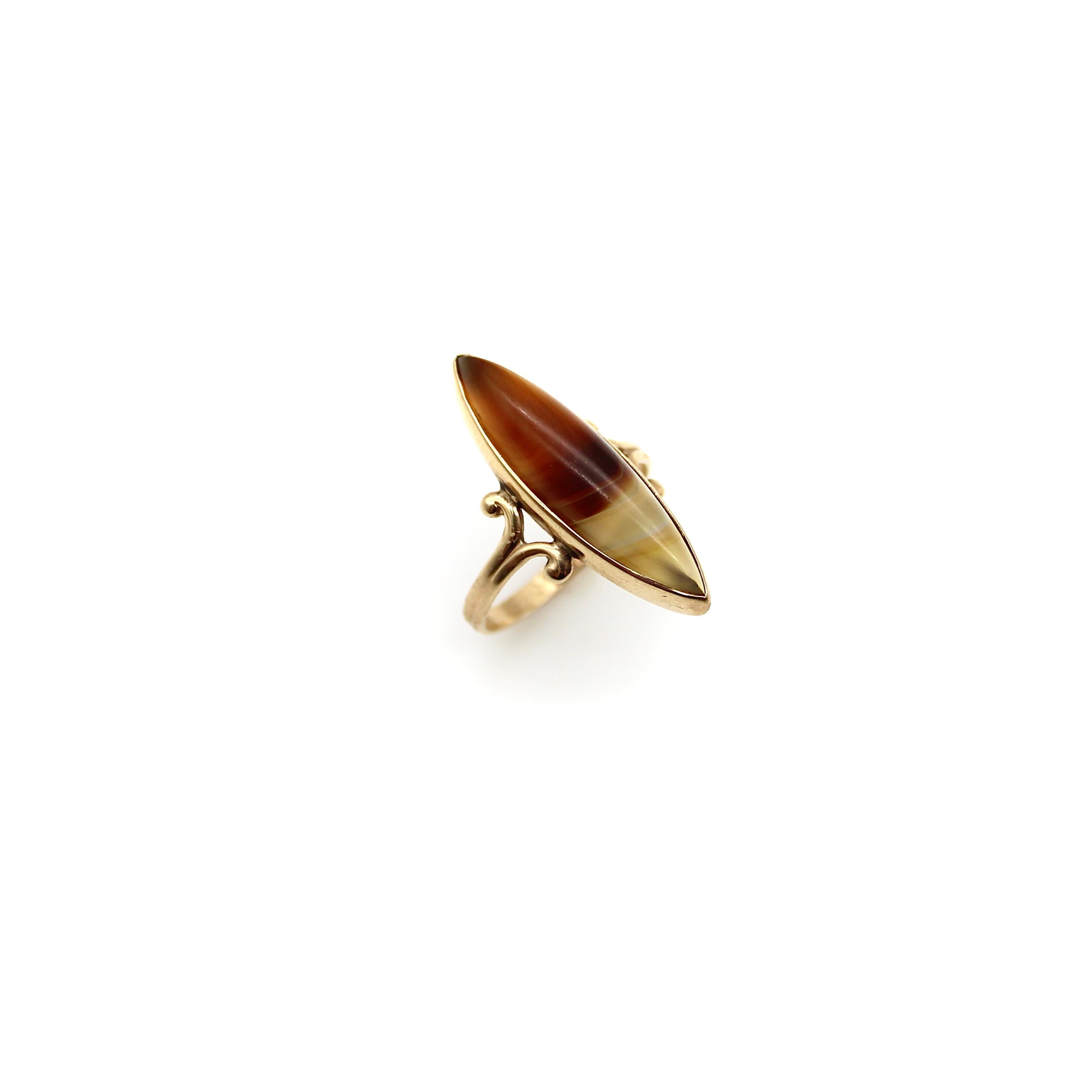 A skinny marquise-shaped banded agate from the Great Northwest decorates the top of this elegant turn-of-the-century ring. The translucent banded agate creates a sliver or boat-like form with its narrow dimensions. The agate is soft to the touch and