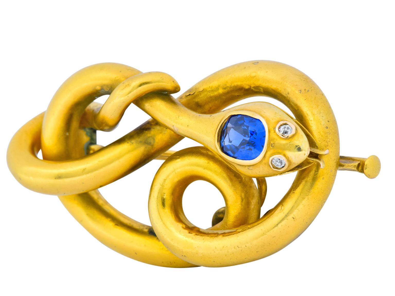 Brooch designed as matte gold snake intertwined upon itself

With a bezel set cushion brilliant cut Kashmir sapphire weighing 0.80 carat, transparent and vibrant blue in color with no indications of heating

Accented by two old European cut eyes