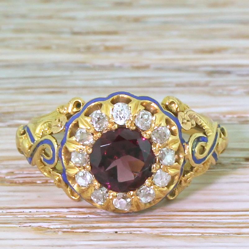 A flamboyantly beautiful Victorian garnet ring. The bright and richly coloured centre stone is surrounded by twelve lively old cut diamonds. The stunningly ornate surround features a swirling ribbon of sky blue enamel, leading to a slim D-shaped