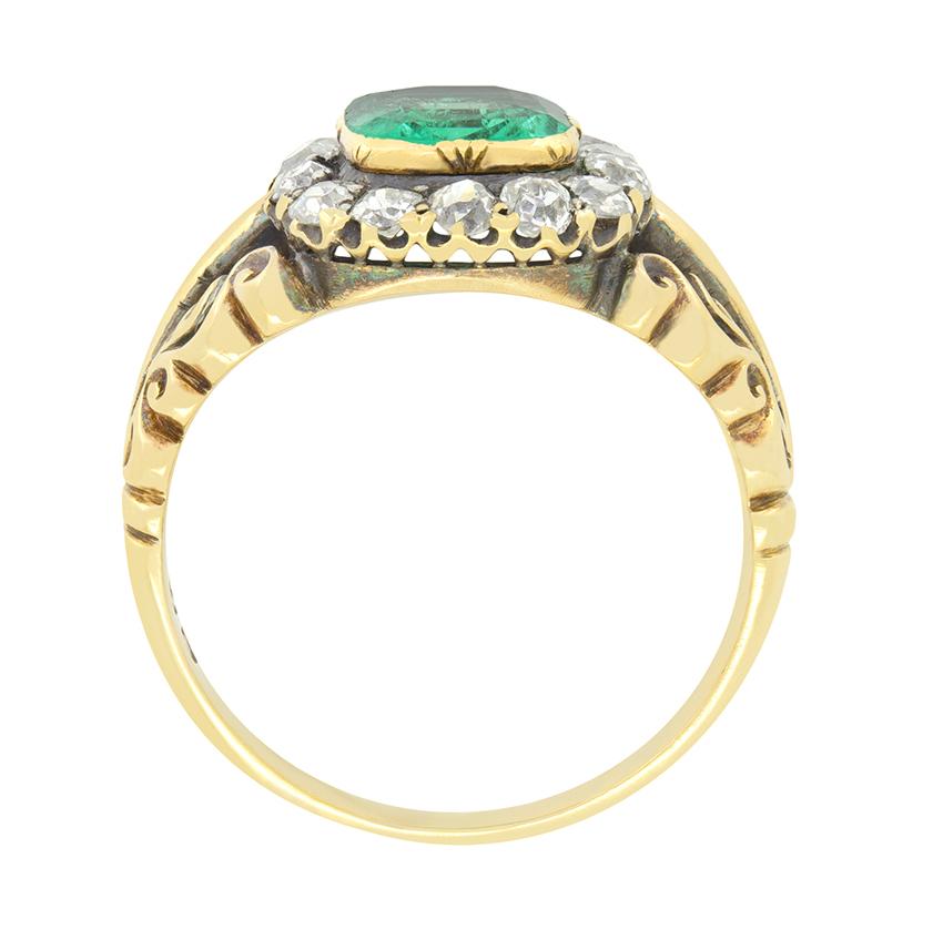 Dieser bezaubernde Clusterring zeigt ein klassisch viktorianisches Design. In seinem Zentrum sitzt ein 1,20 Karat schwerer Smaragd, der in einer ungewöhnlichen Asscher-Schliffform geschliffen und in 18 Karat Gelbgold gefasst ist. Der zentrale Stein