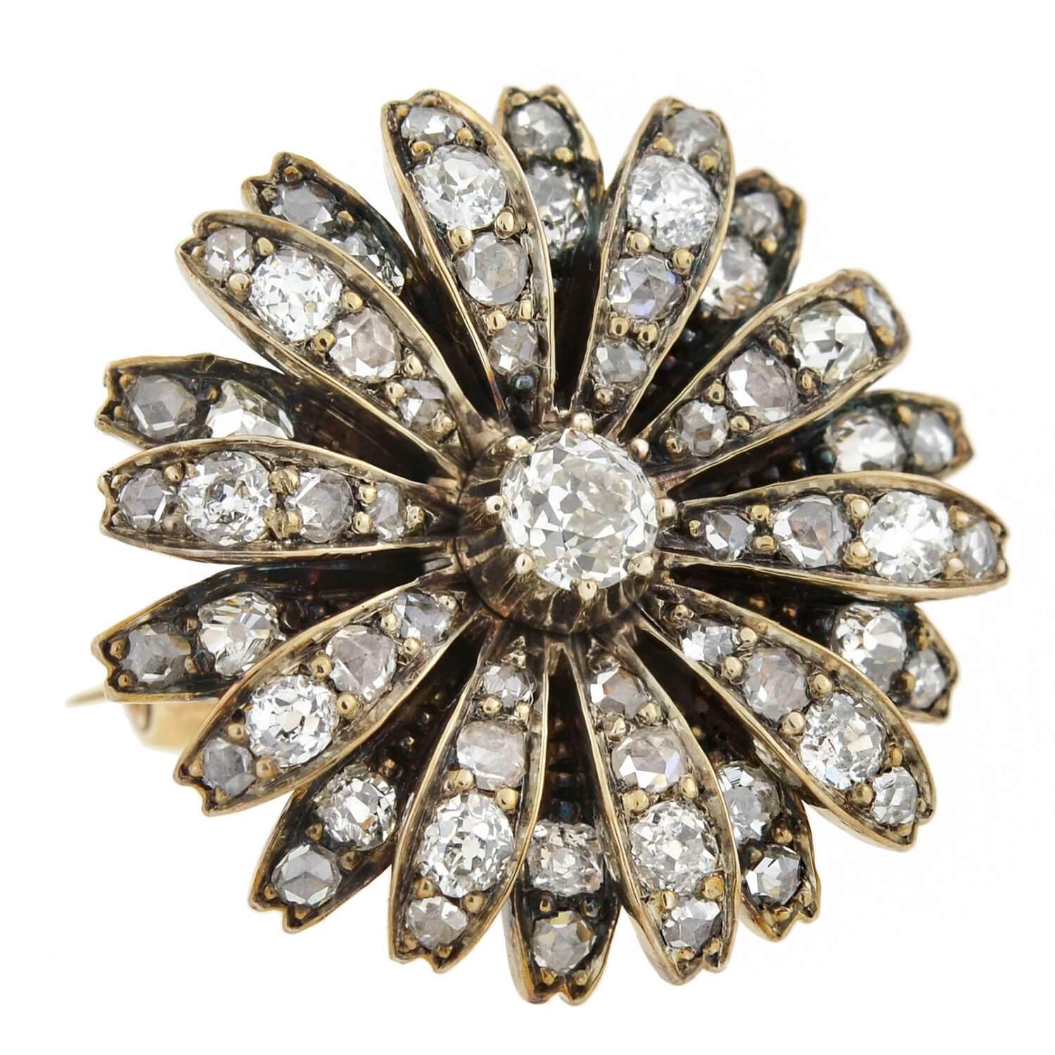 A beautiful diamond flower pin/pendant from the Victorian (ca1880) era! This exquisite sterling topped 14kt yellow gold piece is adorned with a double layer of diamond encrusted petals that surround a larger old Mine Cut diamond at the center. A
