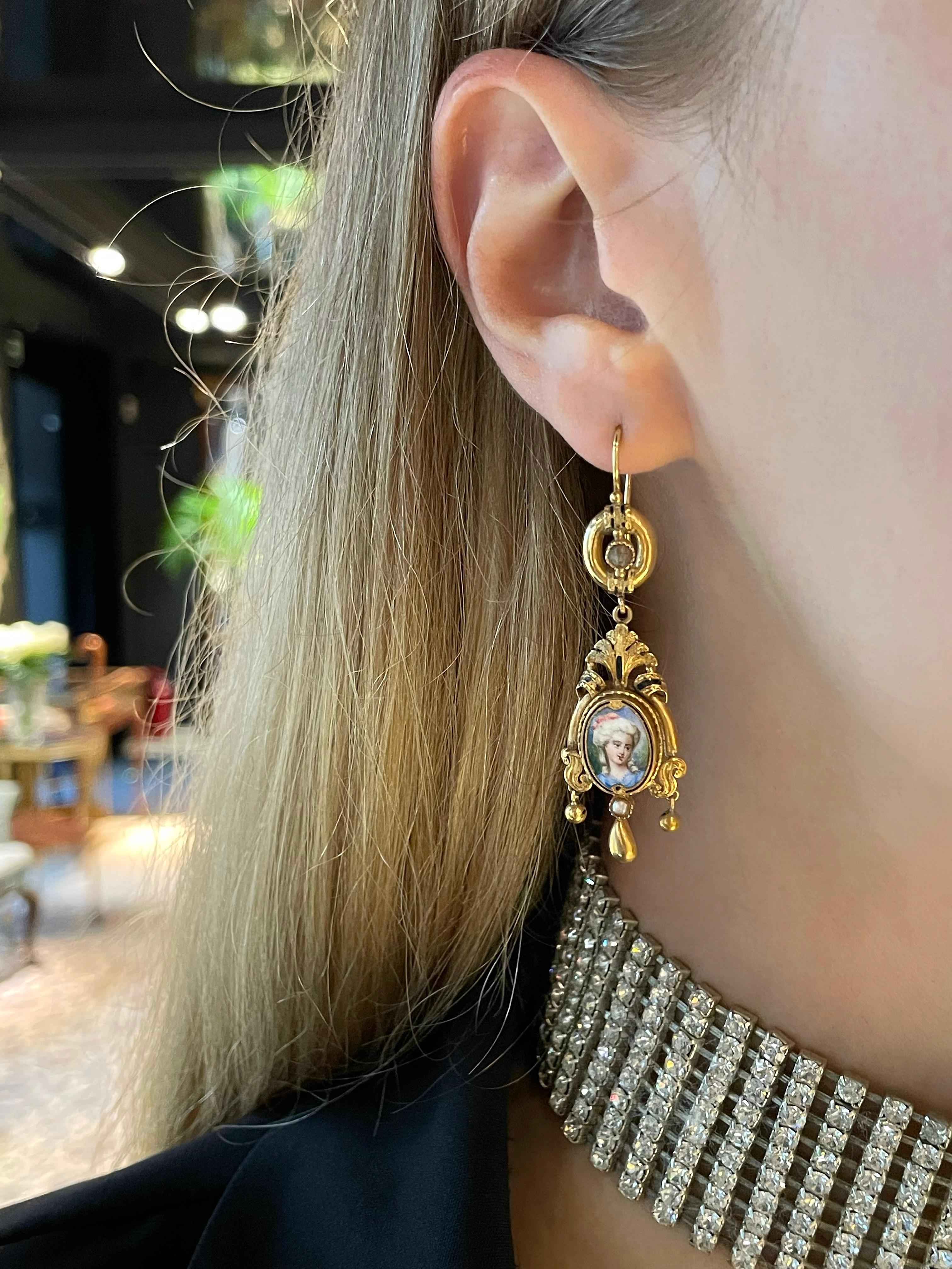 This is a pair of lovely Victorian dangle earrings crafted in 14K yellow gold. The piece features detailed vivid miniature portraits of ladies painted on porcelain. 

These earrings are adorned with seed pearls and black enamel (average condition -