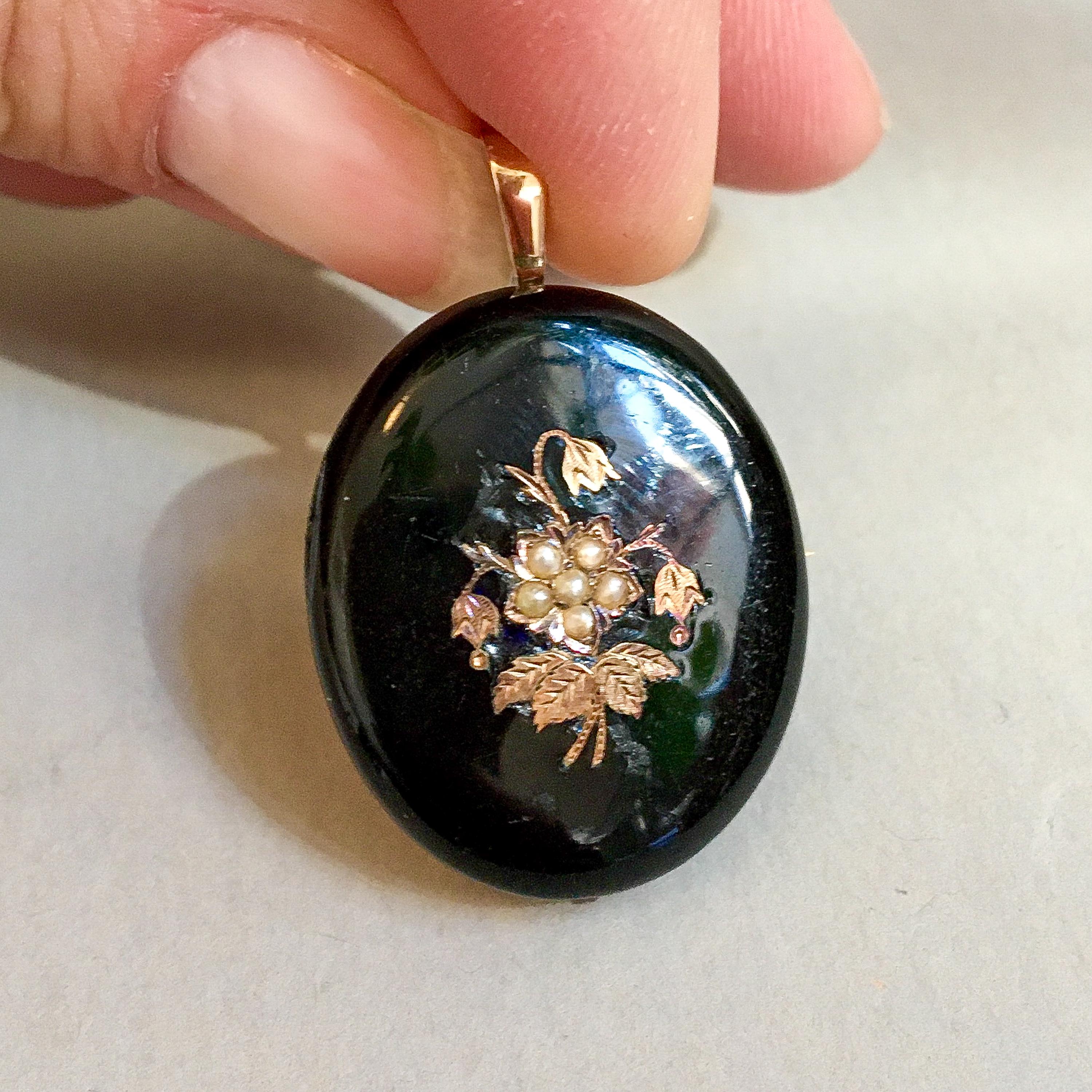 An antique 19th century black onyx pendant created with pearls set in a gold floral decor. The oval-shaped brooch pendant is set with golden leaves and a floral pattern inlaid with six seed pearls in the center. The bail at the top is made in 14