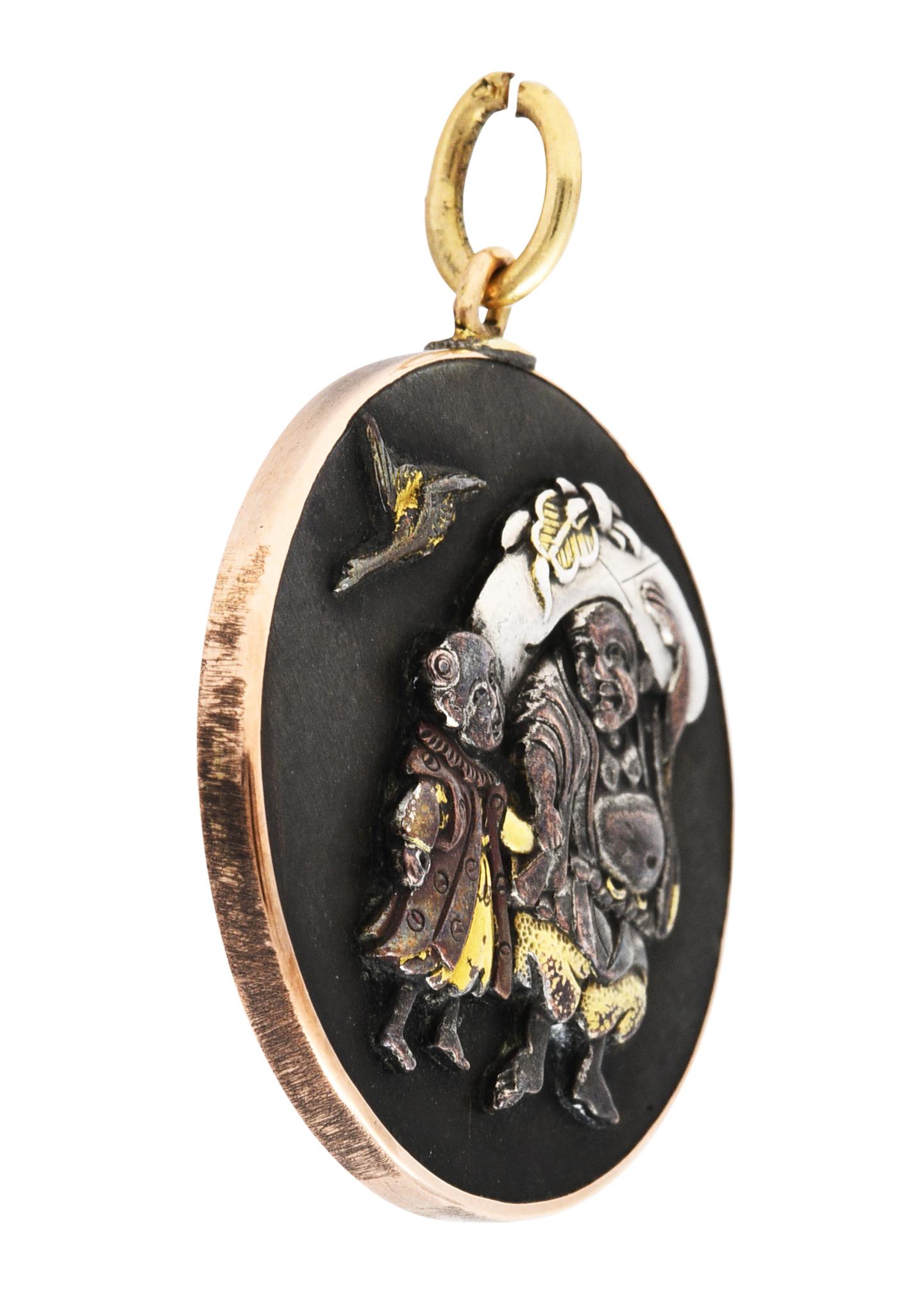 Circular pendant features a round shakudō billon

Heavily oxidized with gold and silver appliqué

Depicting a jovial man and his daughter carrying luggage with a bird soaring overhead

Bezel set in a gold surround and backed by silver

Tested as 14