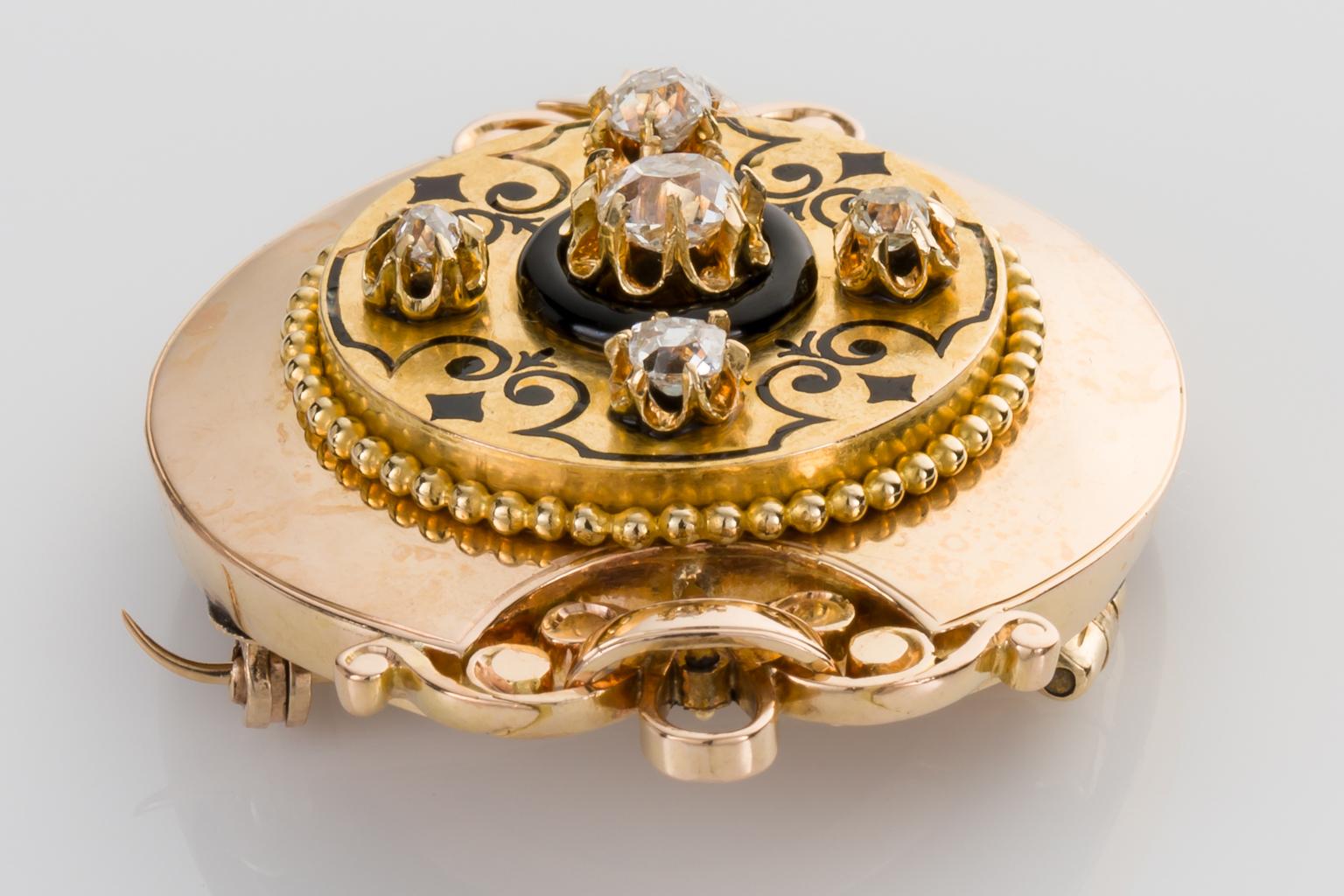 An ornate Victorian memory brooch set with bright old cushion cut diamonds weighing approximately 0.20cts claw set within detailed scalloped cups surrounded by black enamel scrollwork with the central diamond surrounded by an onyx ring. Detailed