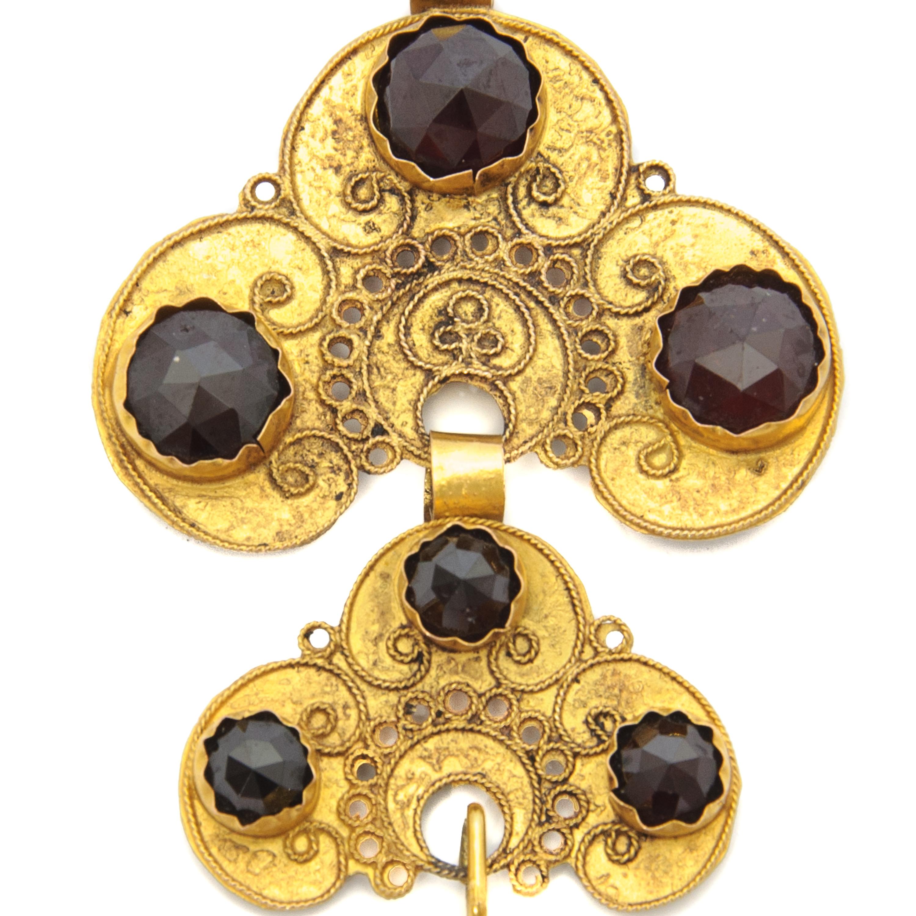 Beautiful 14 karat yellow gold pendant set with seven faceted cut garnet gemstones. The pendant has cloverleaf-shapes. The pendant is open worked and has swirls and curls on both sides. At the front the gold is set with seven beautiful faceted