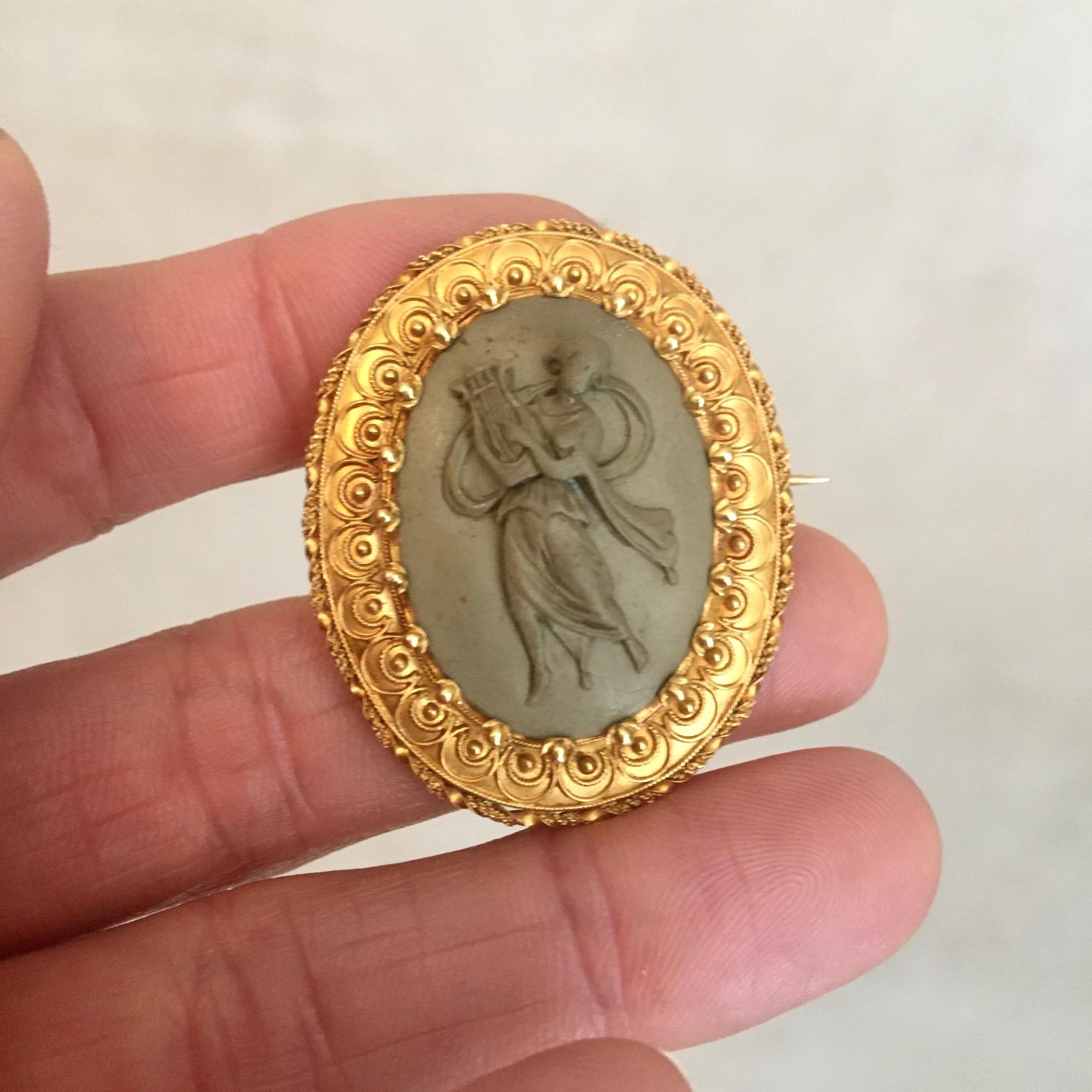 An antique 19th century high relief lava cameo brooch created with a 14 karat yellow gold frame. This gorgeous carved high relief depicts a graceful muse playing her lyre. The gold border is finely detailed with twisted ribbon around the edge, rope
