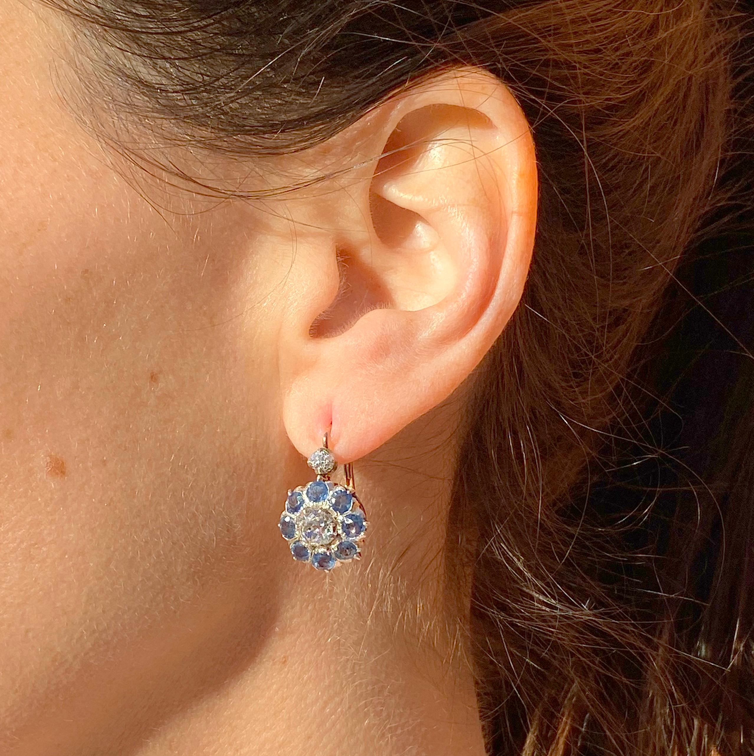 A sensational pair of antique earrings. Each cluster is set with an (approx.) 0.65 carat old mine cut diamond at the centre, both extraordinarily white, bright and lively. Eight cornflower blue natural sapphires surround the centre stone in a fine,