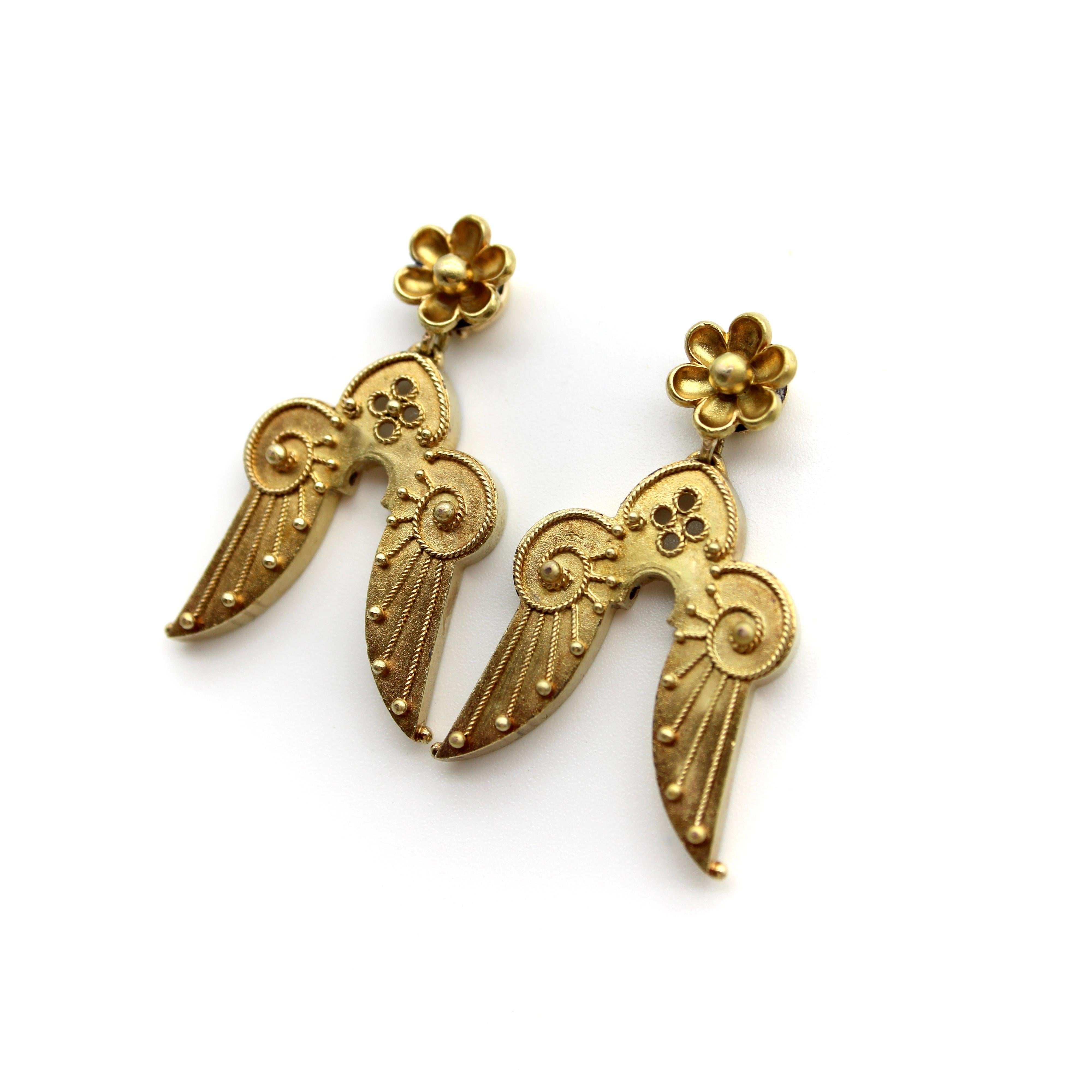 Circa the Victorian era, these 14k gold Etruscan Revival earrings are reminiscent of angel wings. Suspended from golden flowers, the earrings are finely detailed, adorned with twisted wirework and gold beading. Their angelic motif has a double