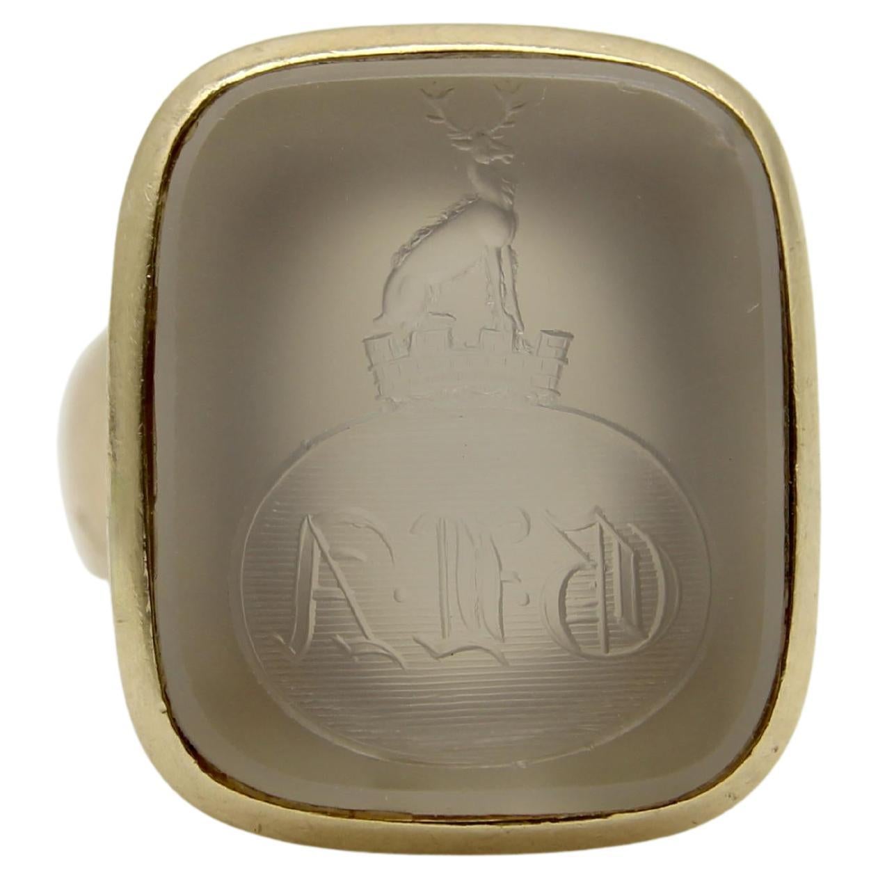 Delicately carved into a quartz tablet, this family crest intaglio is the image of a stag standing on top of a crown and castle. Below it are the letters GLA in an oval, written in a highly gothic script with striped texture behind it. The quartz