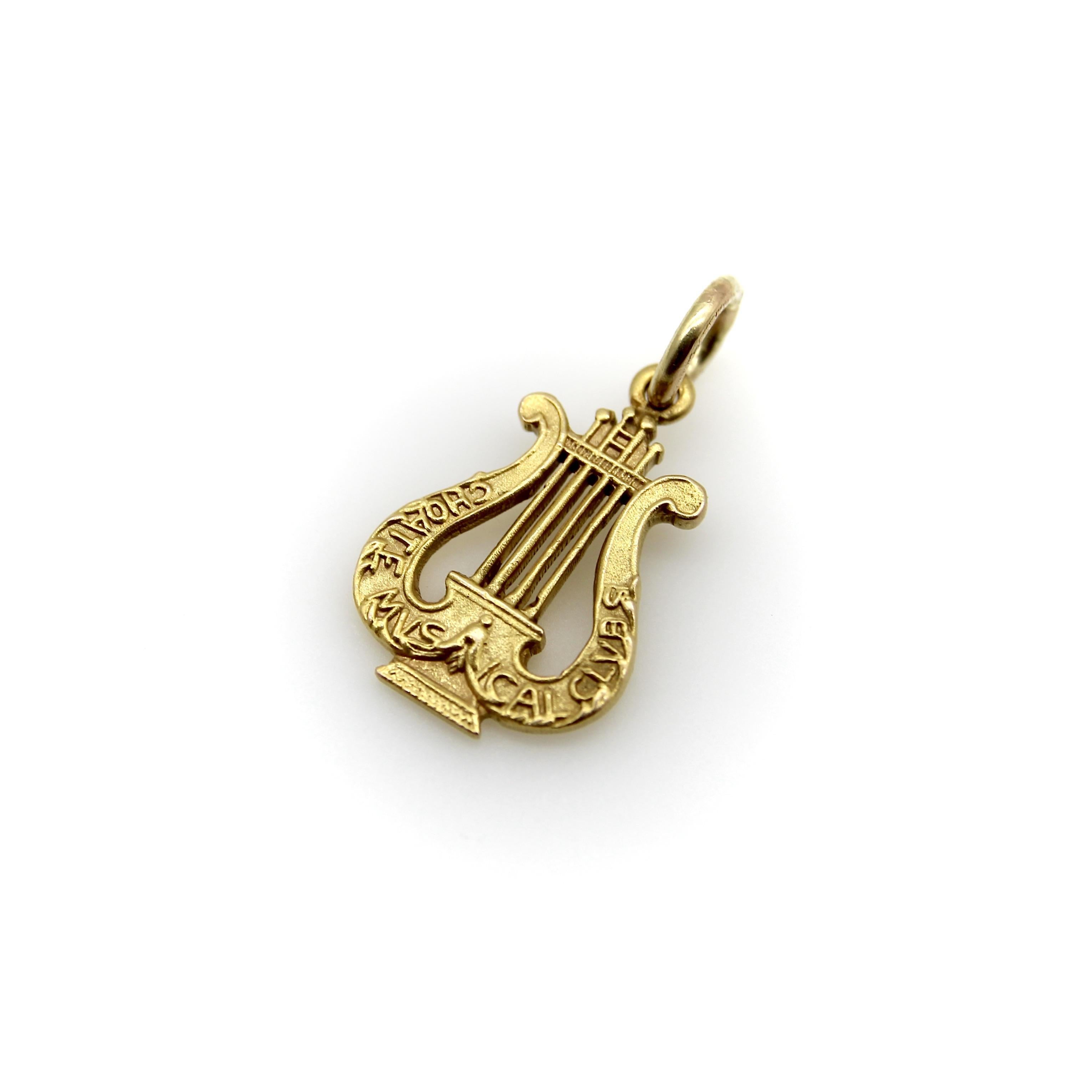 Ce pendentif en or 14 carats a la forme d'une lyre musicale et porte l'inscription 