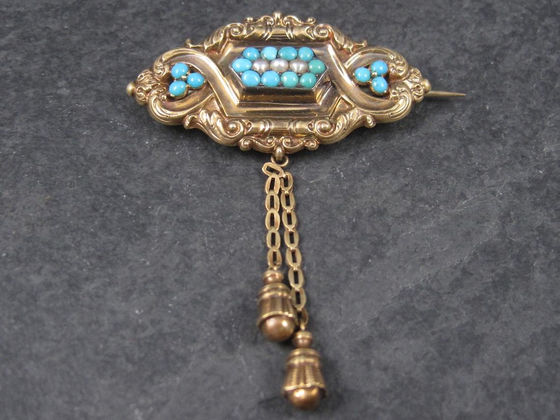 This gorgeous, ornate victorian brooch is 14k gold.
It features 16 natural turquoise and 3 natural pearls.

The 14k gold chain/dangles, though antique, are not original. They were added to the bail for additional decoration when worn as a brooch.