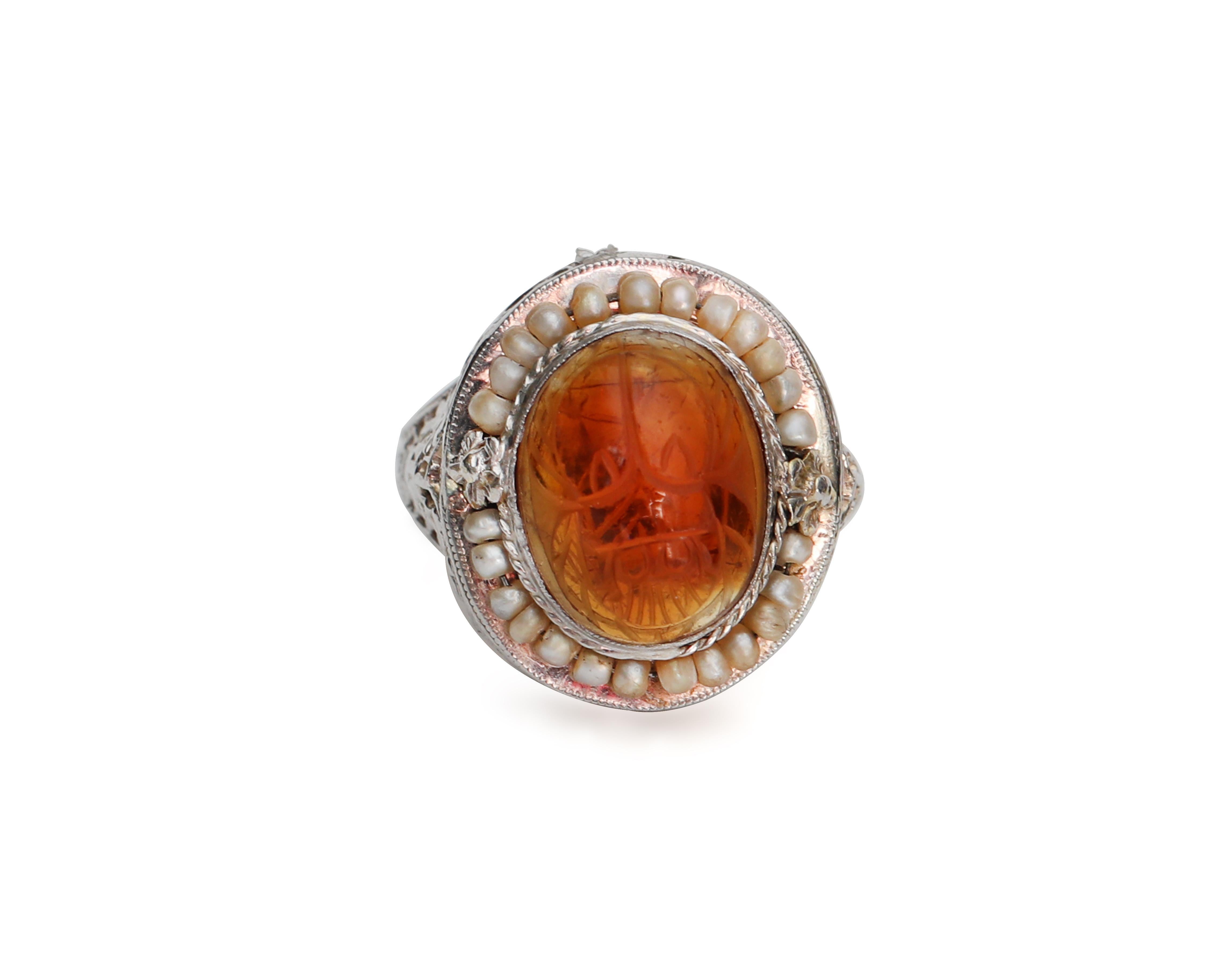 This genuine Victorian beauty features a carved carnelian oval cab surrounded by a dancing seed pearl halo perched atop an intricate 14 karat white gold filigree ring. Although this fine example of late victorian style is over 120 years old, it is