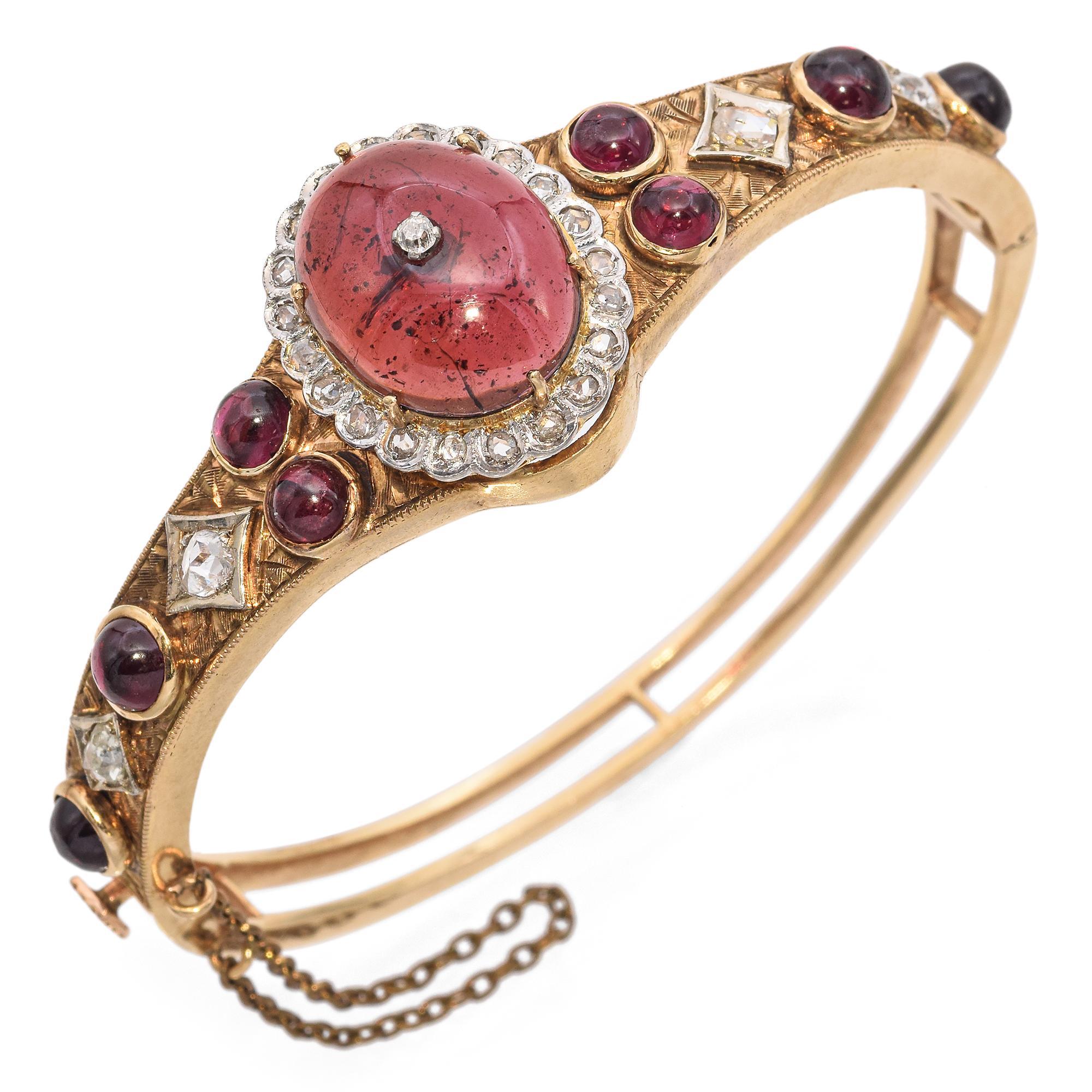 Exquisitely crafted in 14k yellow gold, this Victorian bangle bracelet showcases a striking red cabochon-cut garnet at its center, weighing 8.61 carats. Surrounding this center stone, a halo of rose cut white diamonds adds a touch of brilliance. The