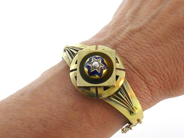 Lovely mourning bangle created in the end of 1800's. It has a compartment for holding something small that reminds you of your beloved one. 
Made of 14k (tested) yellow gold, the bangle holds a button pearl inside a blue enamel six-ray star.
