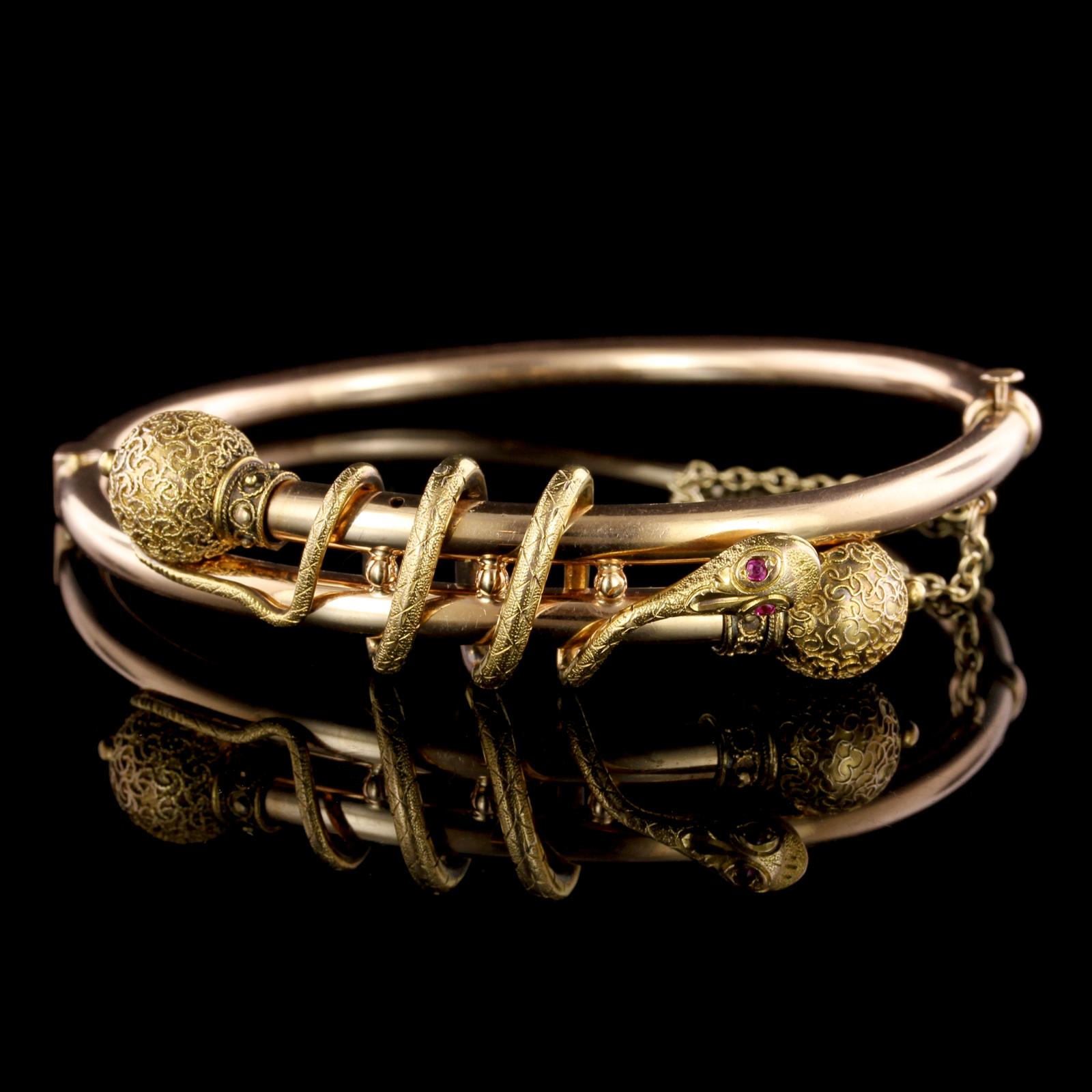 Victorian 14K Yellow Gold Snake Bangle. The bracelet is a hinged bangle with
bead and scroll accents, the snake is set with two round cut ruby eyes, interior
circumference 6 1/2