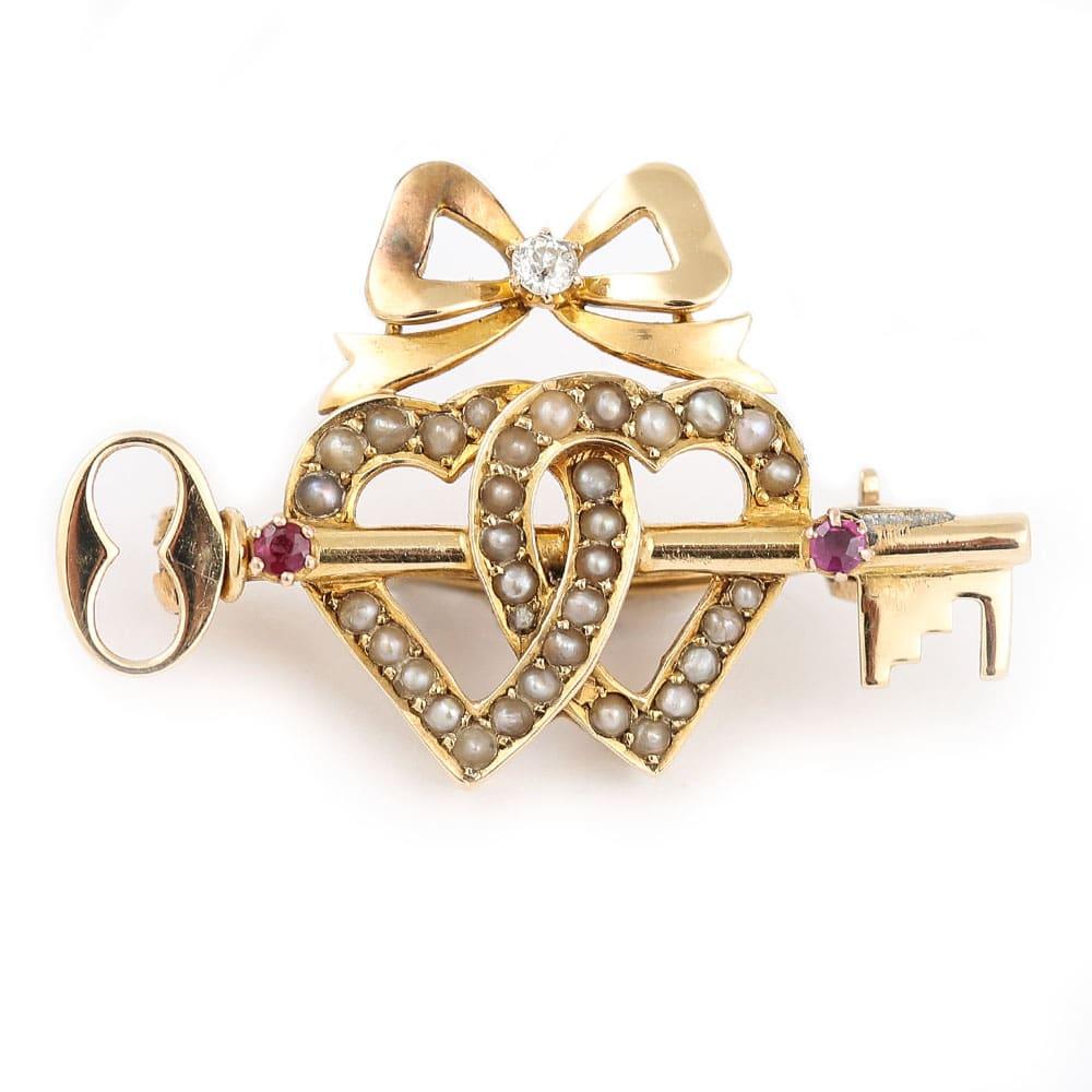 A beautiful Victorian 15 karat yellow gold sentimental brooch. It comprises a pearl double sweet heart, ruby set key and a diamond set bow. A brooch truly loaded with symbolism, this fine and impressive antique sweet heart brooch boasts two split