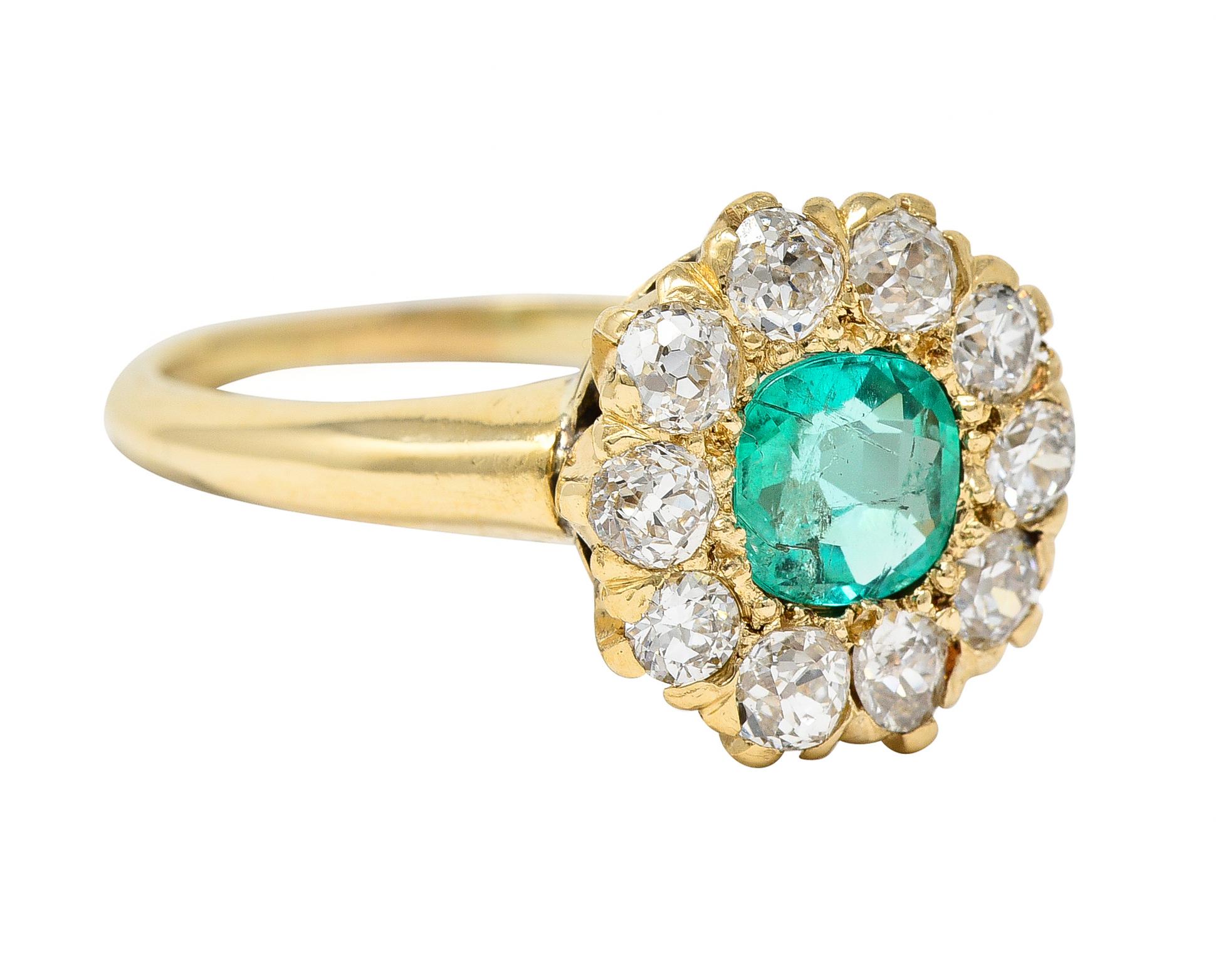 Centering a cushion cut emerald weighing approximately 0.52 carat - transparent light green. Flush set with a halo surround of old mine cut diamonds weighing approximately 1.00 carat total. G/H color with I clarity - prong set and flanked by rounded