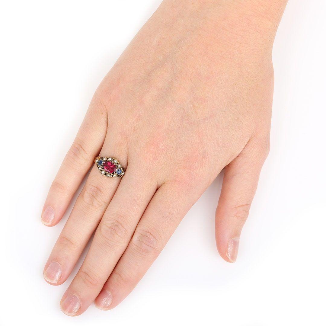 A very pretty Victorian 15ct yellow gold cluster ring set with ten seed pearls and a red paste stone, together with two blue stones. A delightful ring that is reminiscent of the Georgian era with the scrolled setting and engraved shoulder work. Hand