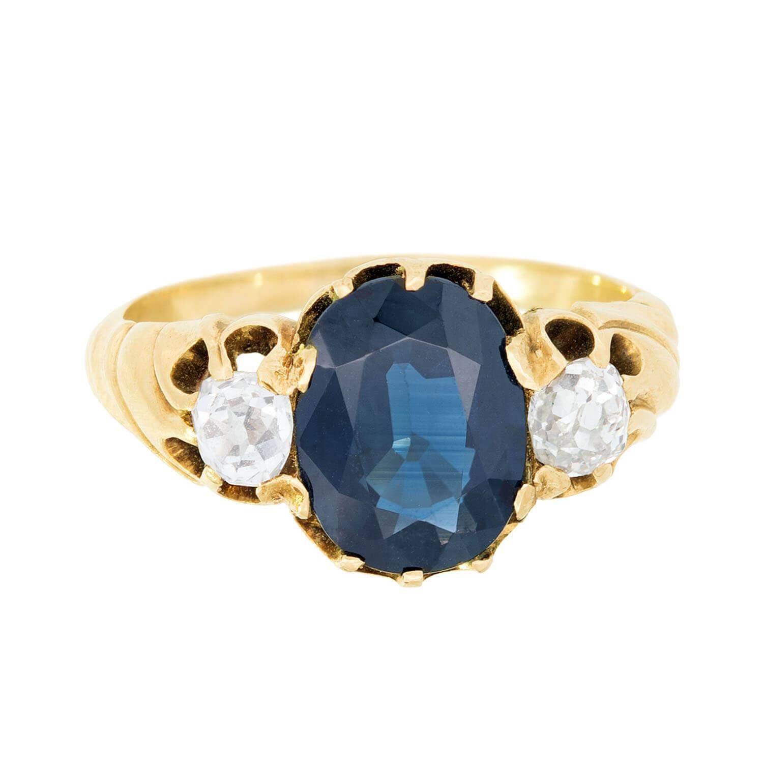 A stunning sapphire and diamond ring from the Victorian (ca1880) era! This lovely piece is crafted in 15k yellow gold and features a vibrant oval cut sapphire at the center framed by two diamonds on either side. The sapphire displays a deep, rich
