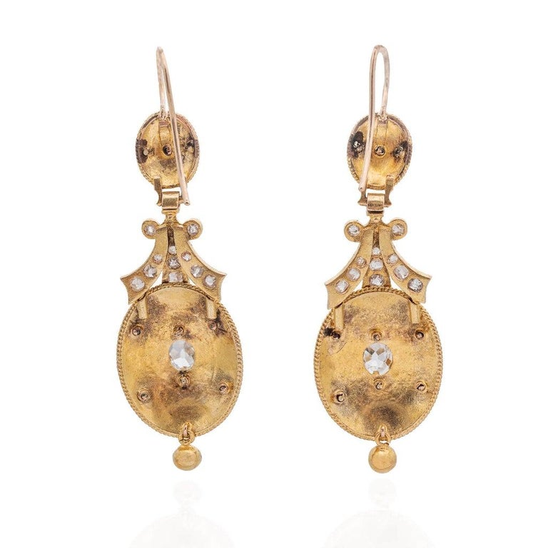 A magnificent pair of earrings from the Victorian (ca1880s) era! Crafted in vibrant 15kt yellow gold, these earrings begin with a simple earring wire atop a stippled oval surmount. The surmount centers a delicate Single Cut diamond in a belcher