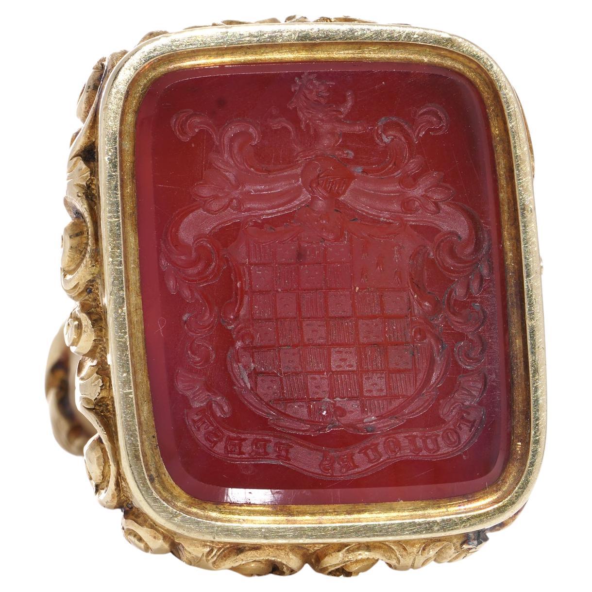 This antique 19th-century seal fob/pendant, crafted from 15kt. yellow gold features a Carnelian intaglio depicting what is possibly the crest of the Carmichael family or clan, along with the French phrase 'Toujours Prest,' which translates to