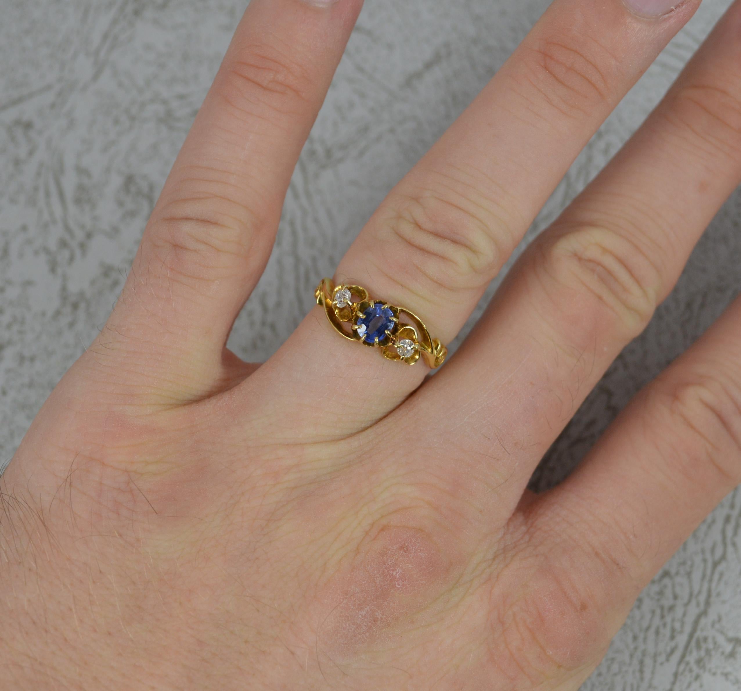 A superb late Victorian fring.
Solid 18 carat yellow gold example.
Designed with an oval shaped blue sapphire to centre. 3.6mm x 5mm approx. Set with an old cut diamond to each side.
Formed on a twist with scroll sides.

CONDITION ; Very good for
